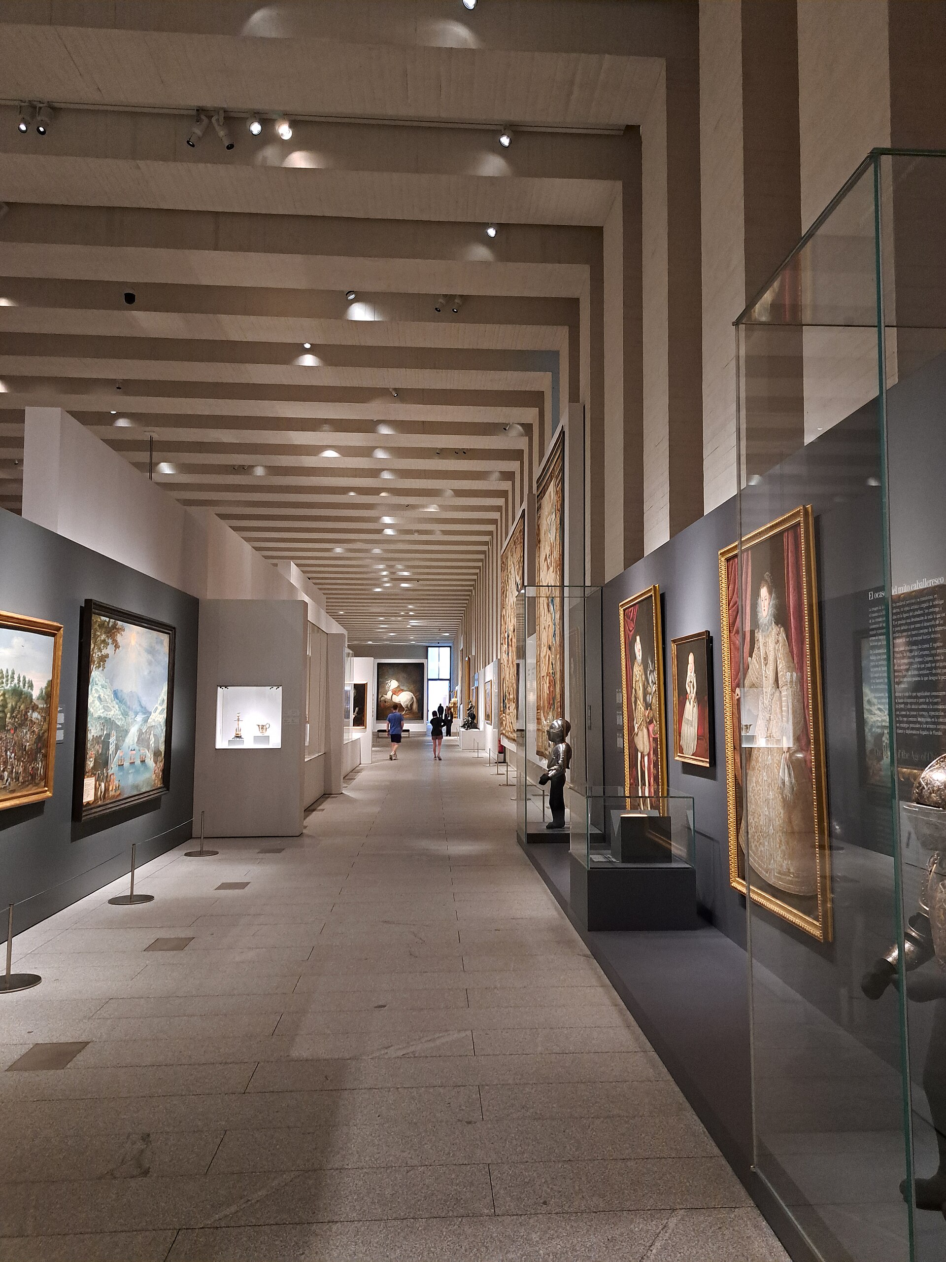 una lunga sala della galeria de las colecciones reales, con il soffitto a travi chiare, ritratti, arazzi e paesaggi alle pareti scure, vetrine con armature e in fondo il cavallo bianco di velazquez