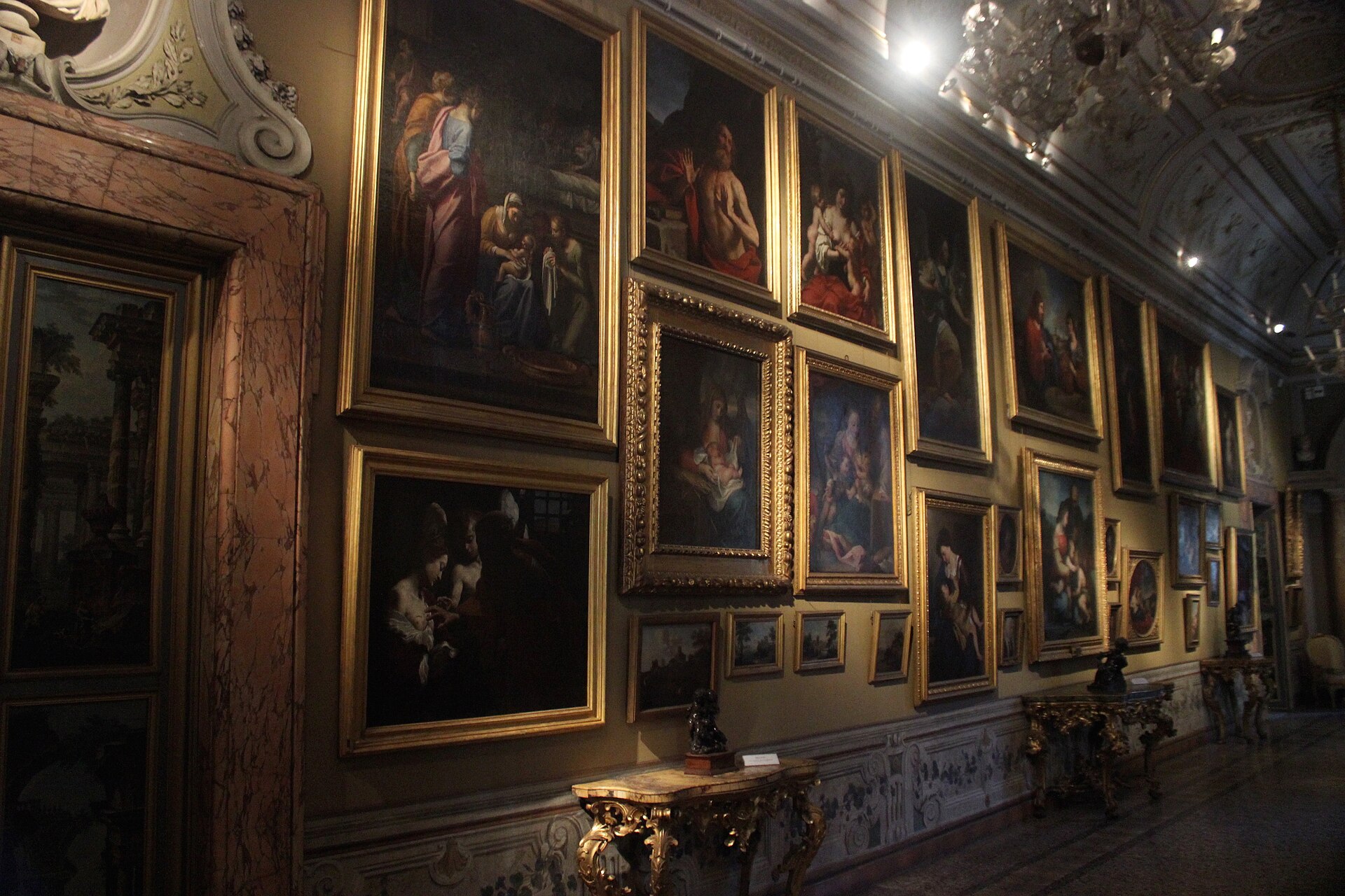 una parete della galleria corsini con i quadri in cornici dorate appesi su piu file fino alla volta, i grandi in alto e i piccoli in basso, sopra consolle intagliate