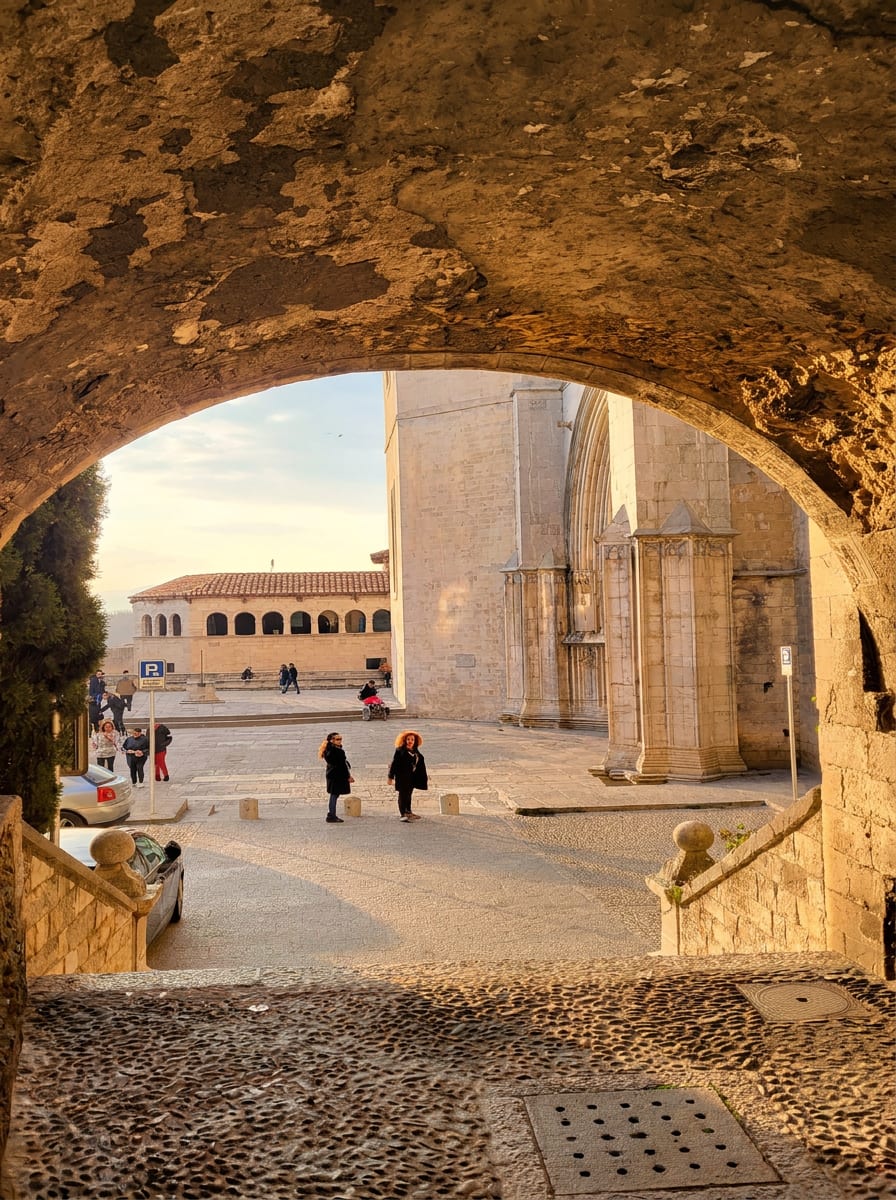 el arco del Portal de Sobreportes en Girona que encuadra la plaza de la catedral con los transeúntes a contraluz