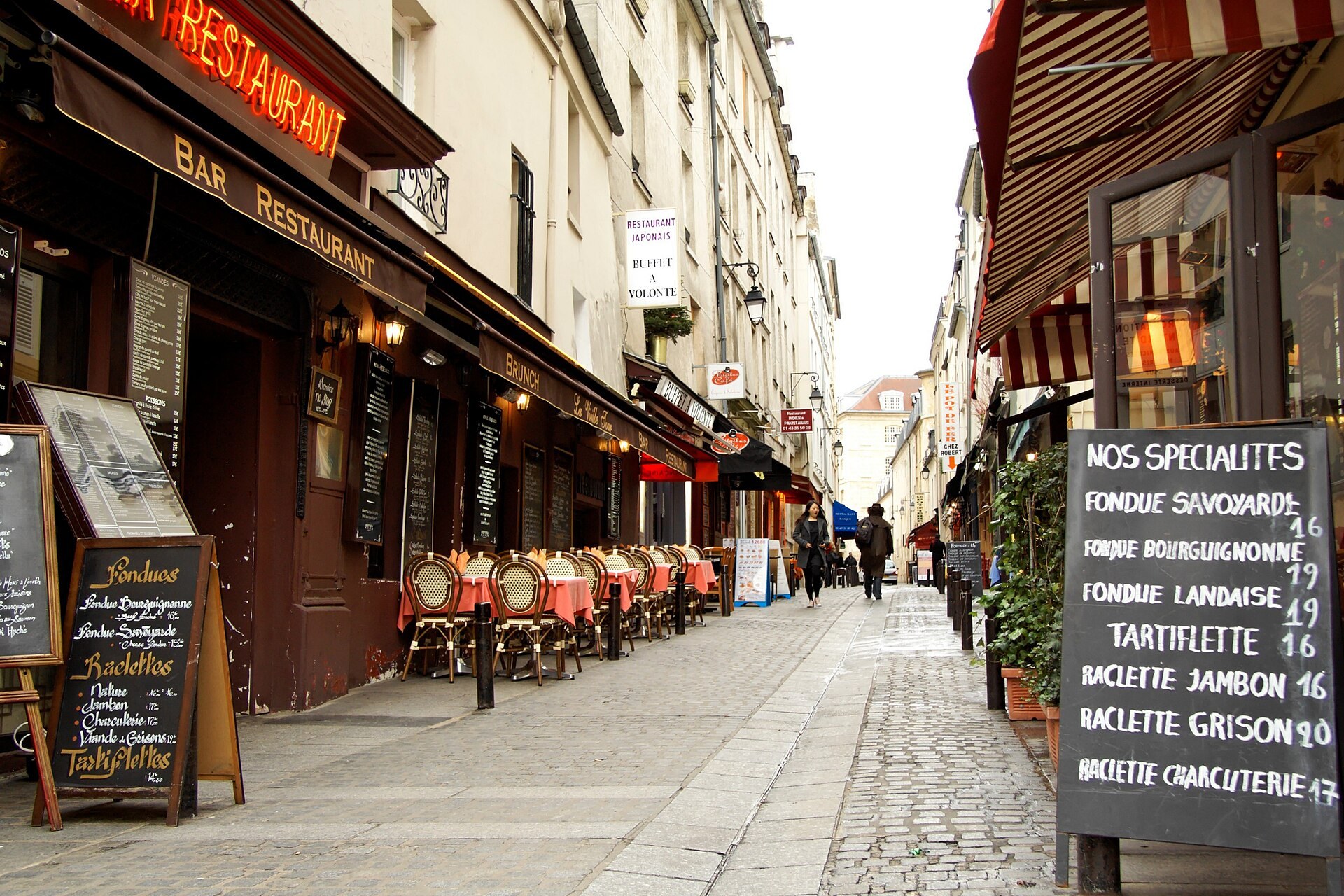 una strada del quartiere latino a parigi con ristoranti all’aperto e lavagne che elencano fondute e raclette a prezzo fisso