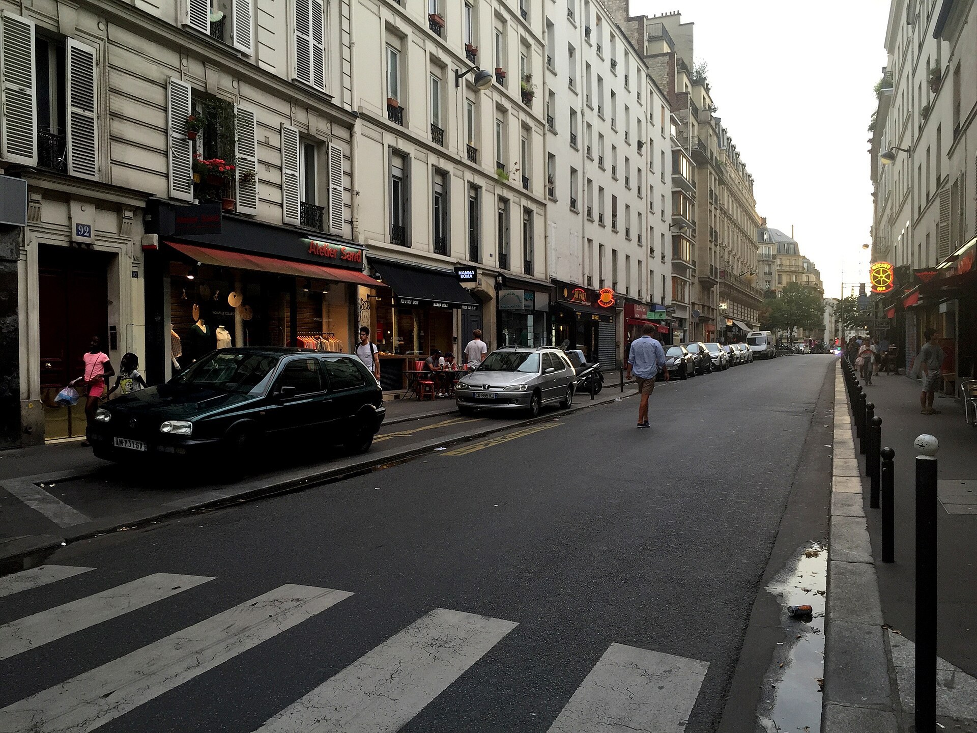 un negozio di abbigliamento con insegna atelier sand su rue oberkampf a parigi, con auto parcheggiate lungo la strada all’imbrunire