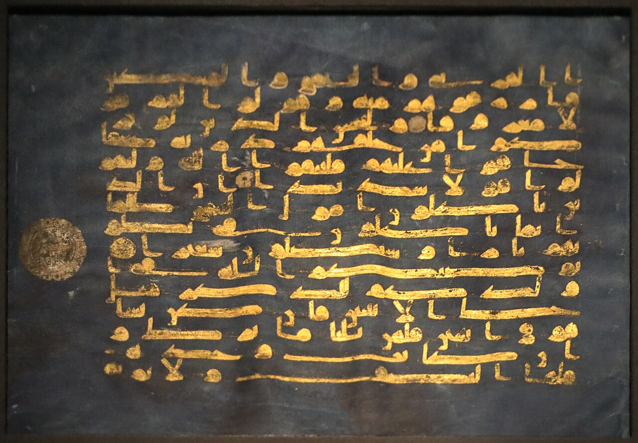 foglio di pergamena tinta di blu scuro con il testo coranico scritto in oro in caratteri cufici larghi e squadrati, e un medaglione circolare sbiadito sul margine sinistro
