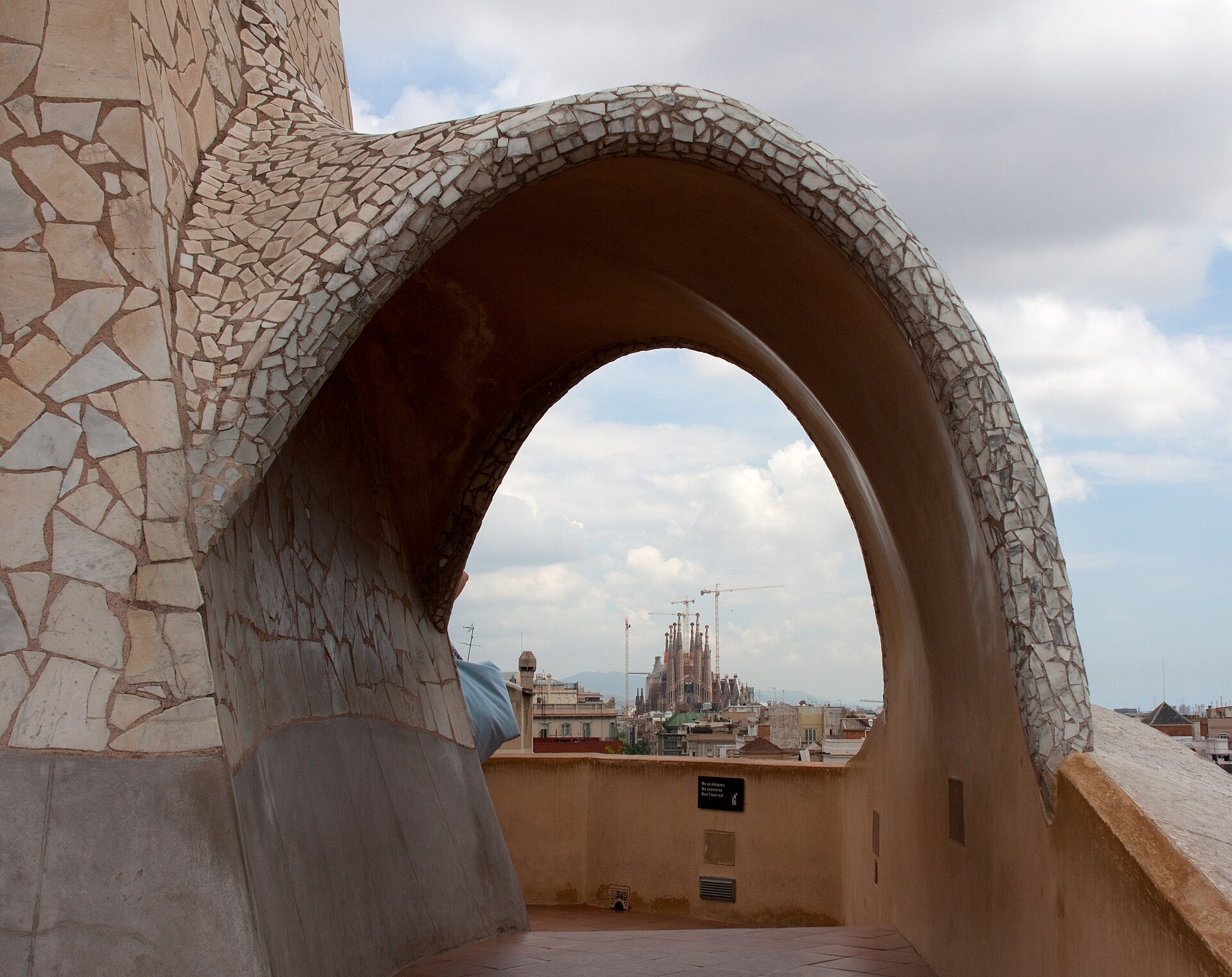 un arco rivestito di cocci bianchi sul tetto della pedrera che incornicia le torri della sagrada familia in lontananza