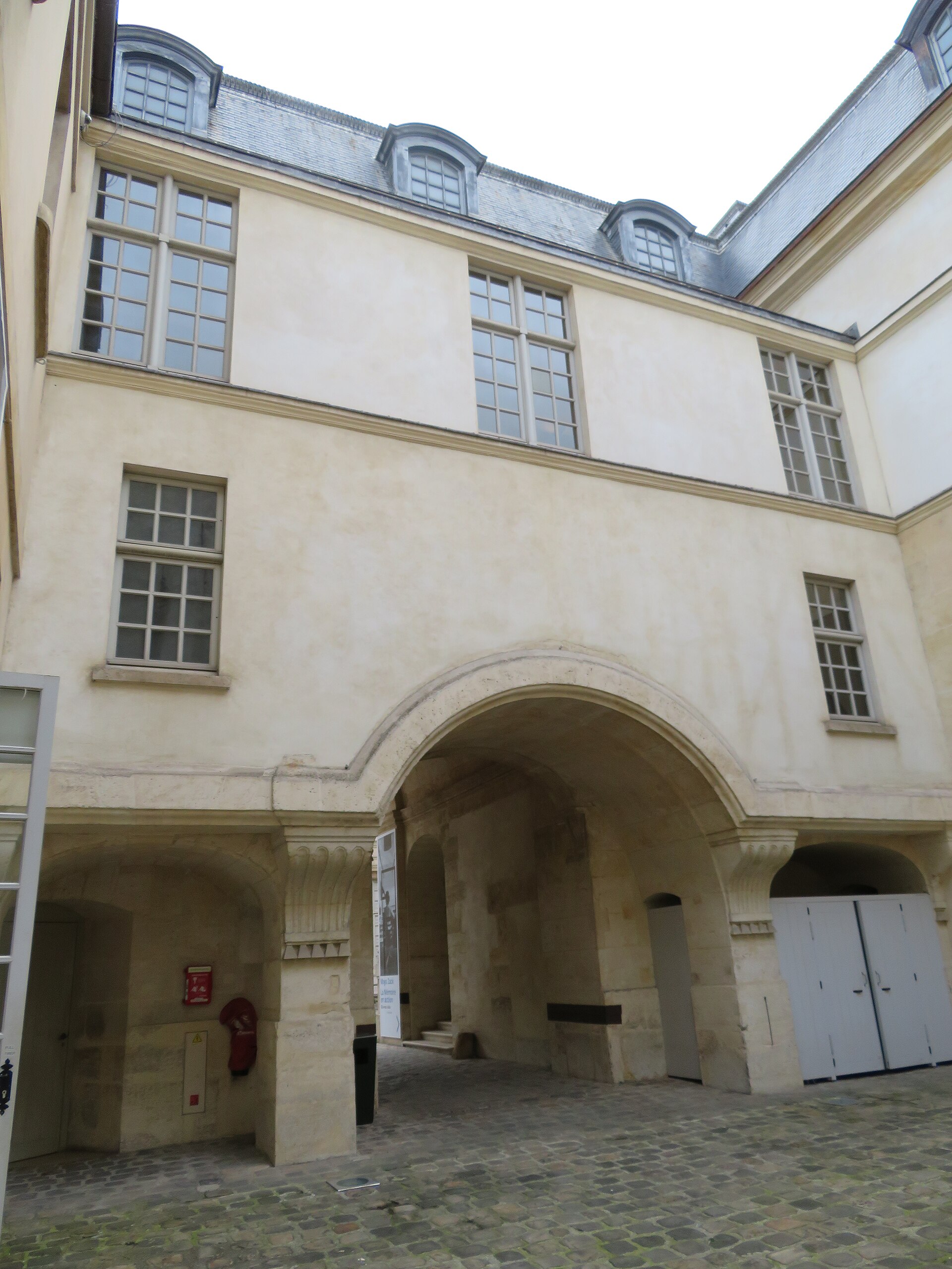 la corticella dell hotel de saint aignan, con il selciato di ciottoli, un grande arco di pietra e le facciate chiare senza decorazioni