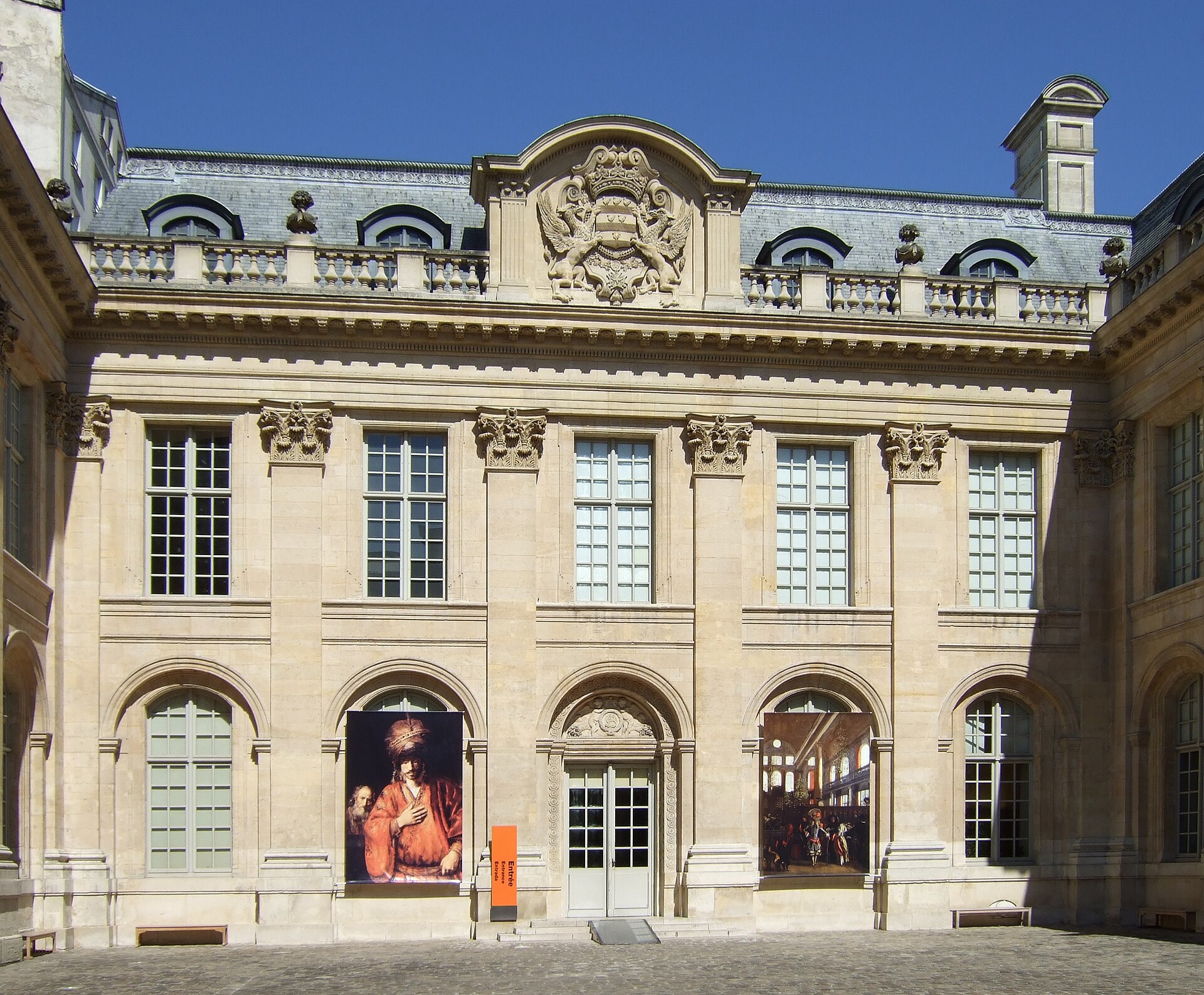 il cortile dell hotel de saint aignan a parigi, con la facciata di pietra chiara a pilastri corinzi, lo stemma scolpito sul frontone e due grandi riproduzioni appese sotto i portici
