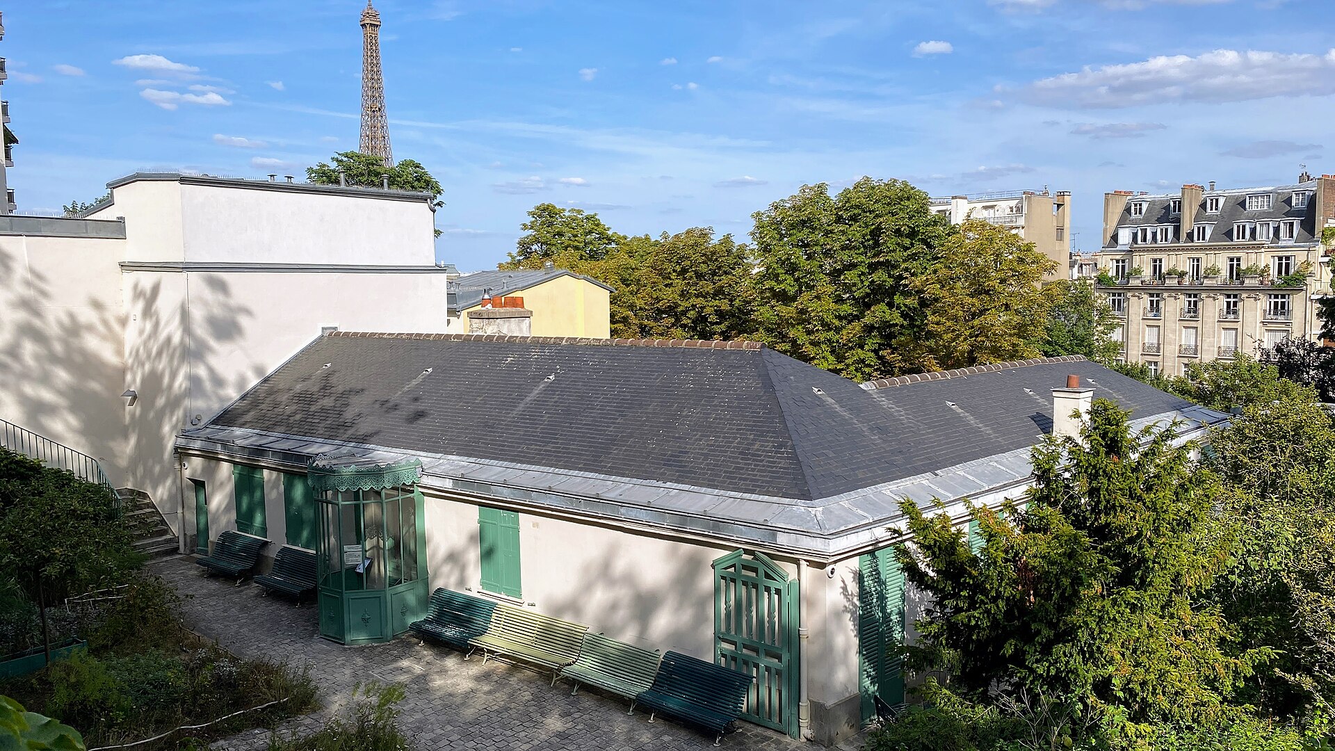 la maison de balzac vista dall alto, con il tetto di ardesia, le persiane verdi, la veranda vetrata dell ingresso e la tour eiffel che si alza contro il cielo a sinistra, sopra un edificio bianco dal tetto piatto