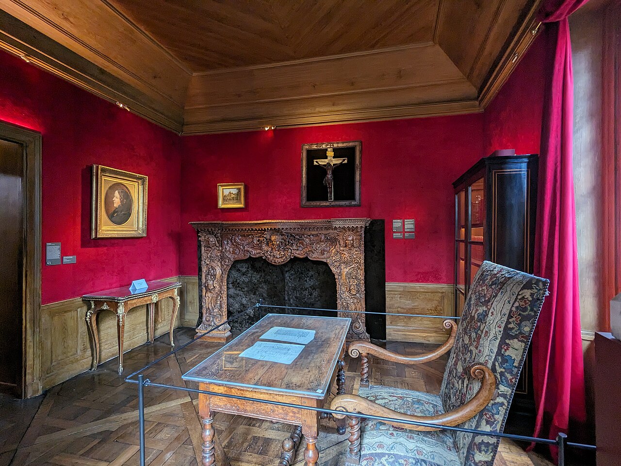 il cabinet de travail della maison de balzac, con le pareti rosse, il camino scolpito, la poltrona imbottita e il tavolo da lavoro protetto da una teca di vetro con due fogli manoscritti