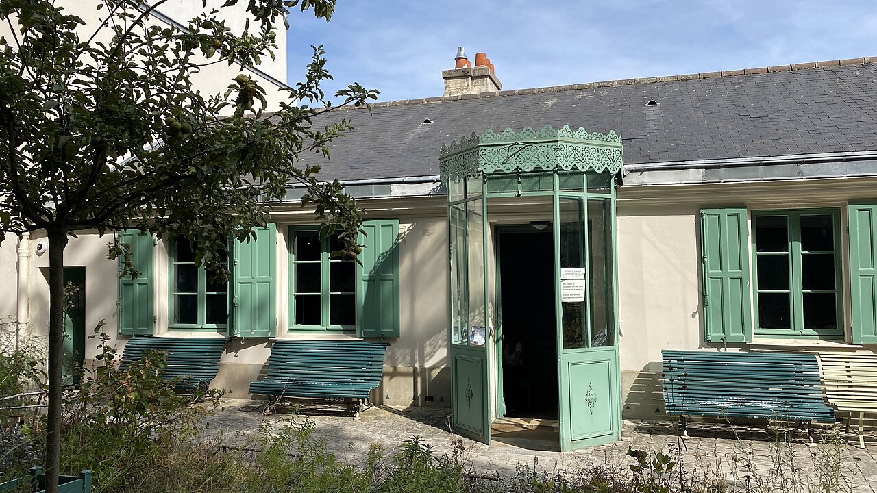 la veranda vetrata verde dell ingresso della maison de balzac vista dal giardino, con la tettoia di ferro traforato, le panchine verde azzurro addossate al muro ai due lati e un melo carico di frutti in primo piano