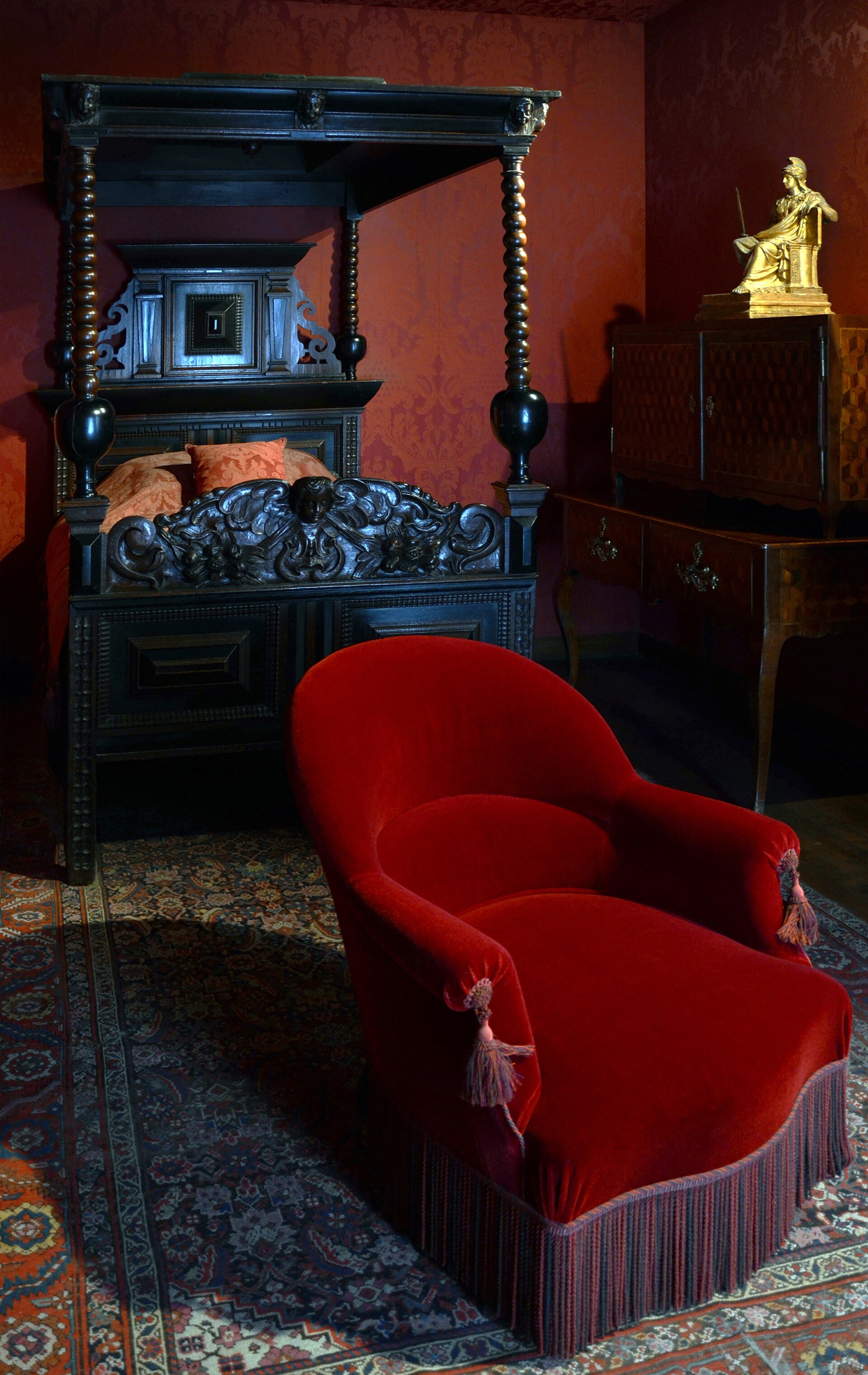 la camera di victor hugo ricostruita al museo, con il letto a baldacchino di legno scuro intagliato, le pareti di damasco rosso, una poltrona di velluto rosso e una statuetta dorata su un mobile
