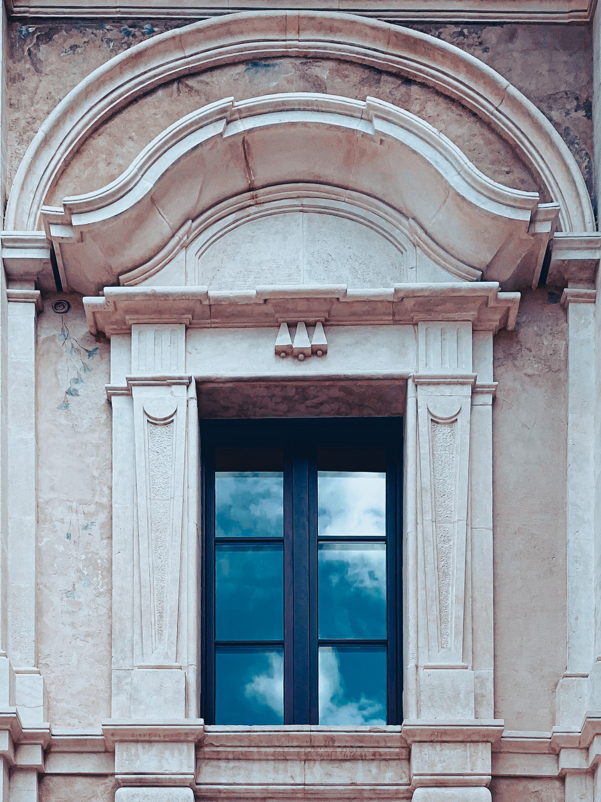 una finestra barocca di palazzo ardinghelli con il frontone mosso a doppia curva e il cielo riflesso nei vetri