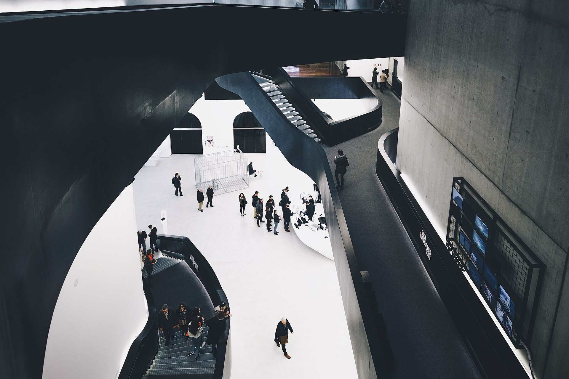 l atrio del maxxi di roma visto dall alto, con le scale nere sospese sopra il pavimento bianco e i muri curvi in cemento