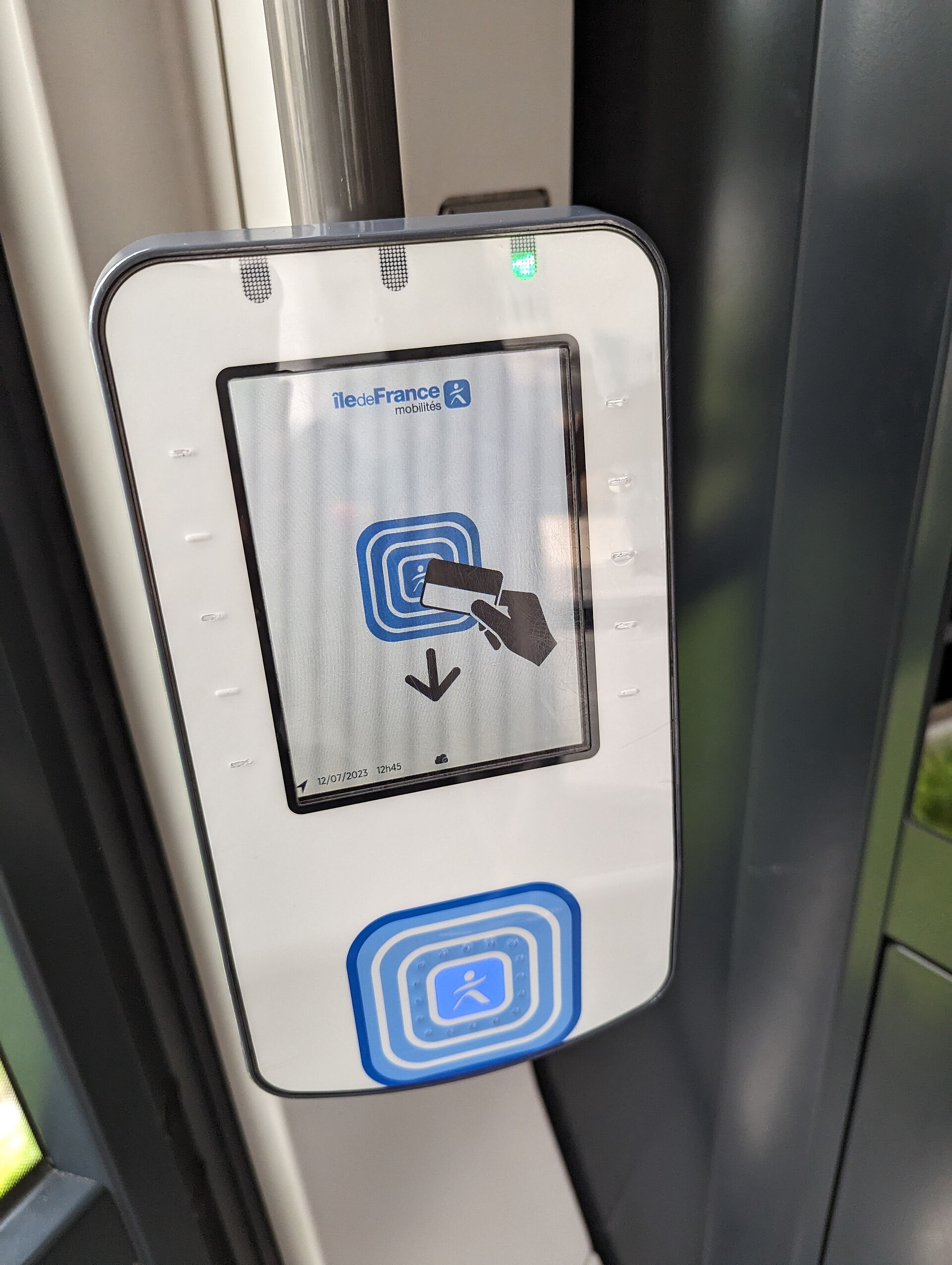 primo piano di un validatore contactless ile-de-france mobilites su un palo del tornello, con lo schermo che mostra l’icona di una carta da avvicinare al lettore