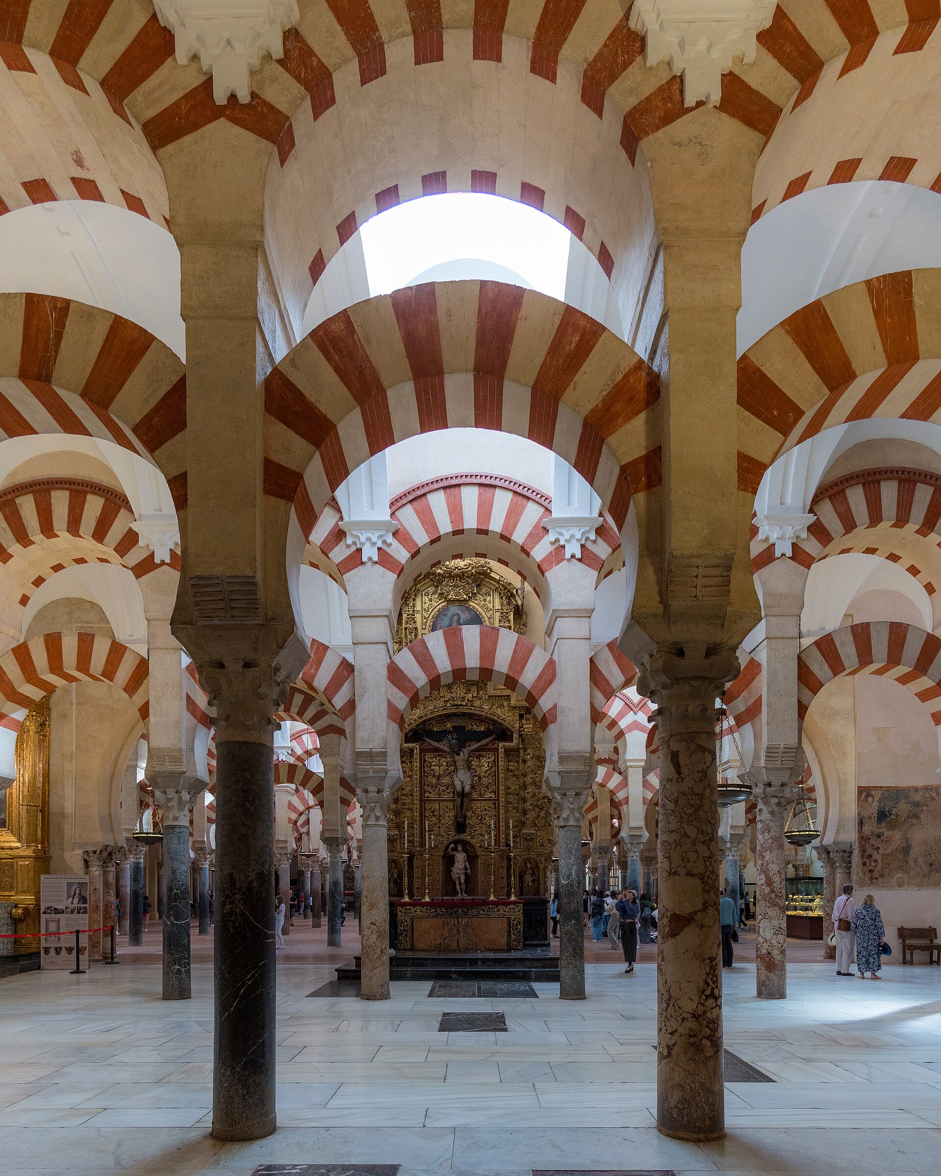 gli archi a strisce rosse e chiare della mezquita di cordoba, e in fondo, fra le colonne, l’altare della cattedrale illuminato