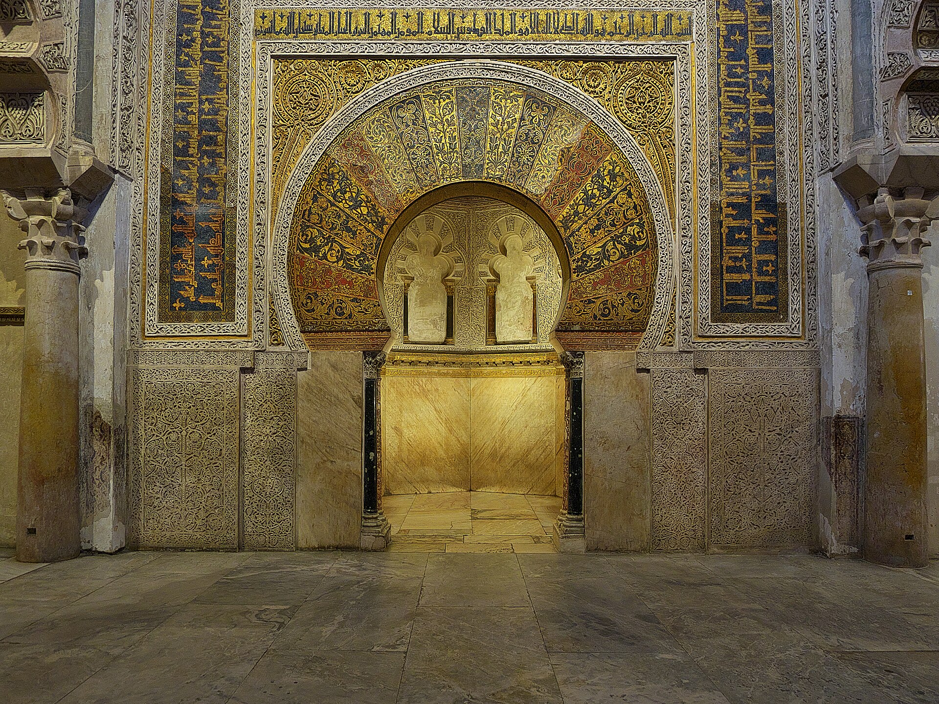 la facciata del mihrab della mezquita di cordoba, con l’arco a ferro di cavallo decorato di mosaici dorati e fasce di iscrizioni
