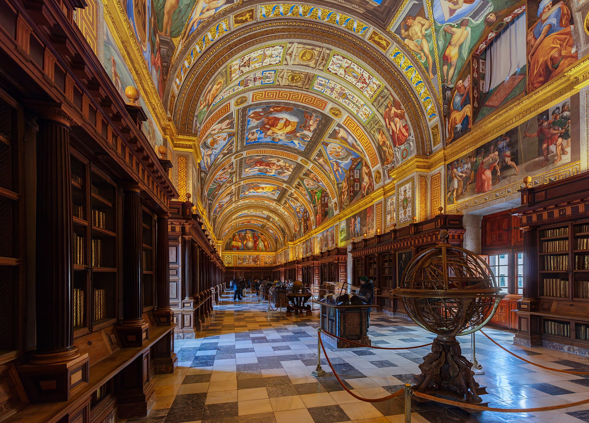 la biblioteca dell’escorial, una lunga sala con gli scaffali di legno scuro, la volta affrescata a colori vivaci, il pavimento di marmo e un globo armillare al centro