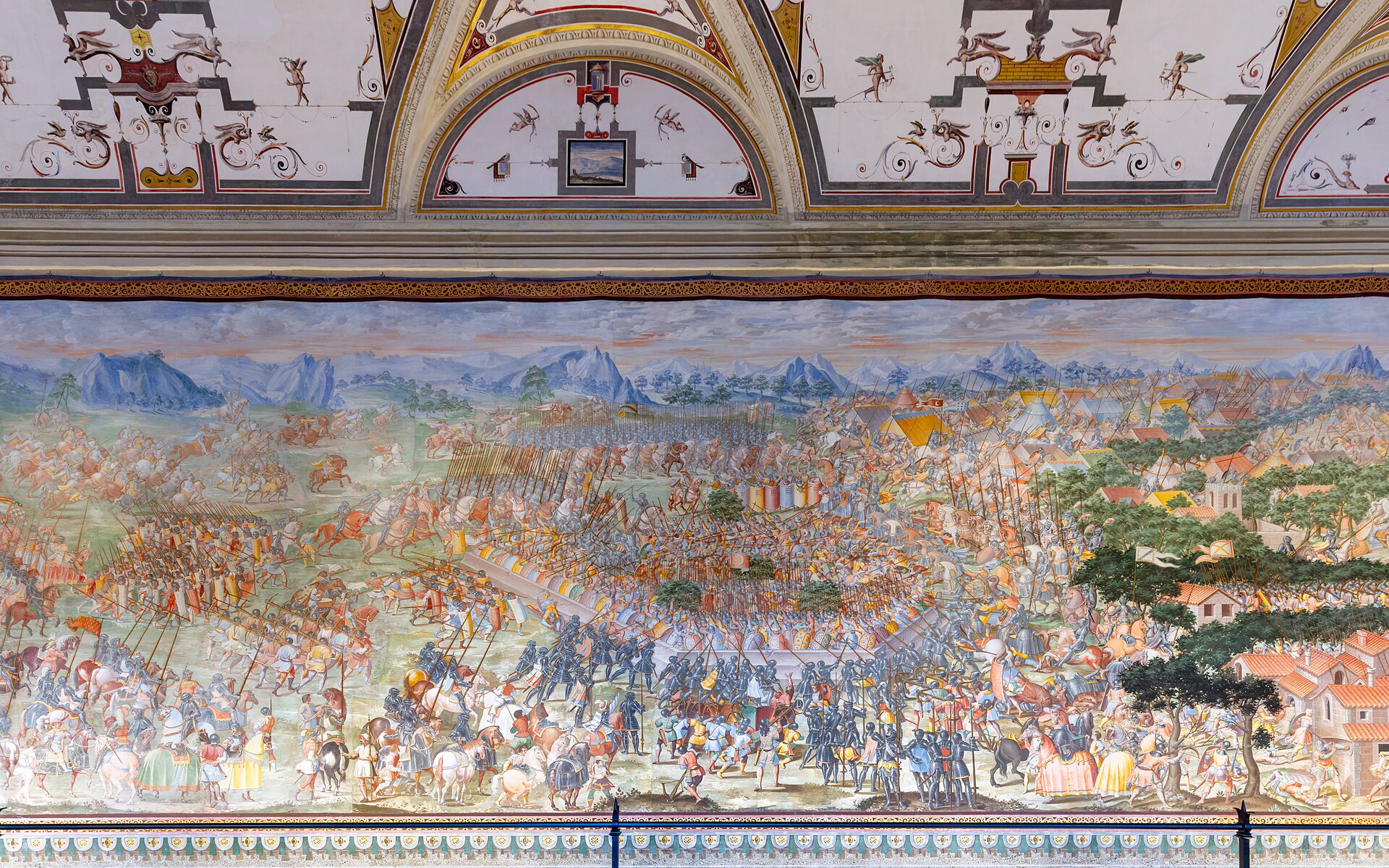 la sala delle battaglie dell’escorial, con un lungo affresco di una battaglia con migliaia di soldati e cavalieri che corre lungo la parete, sotto una volta decorata a grottesche