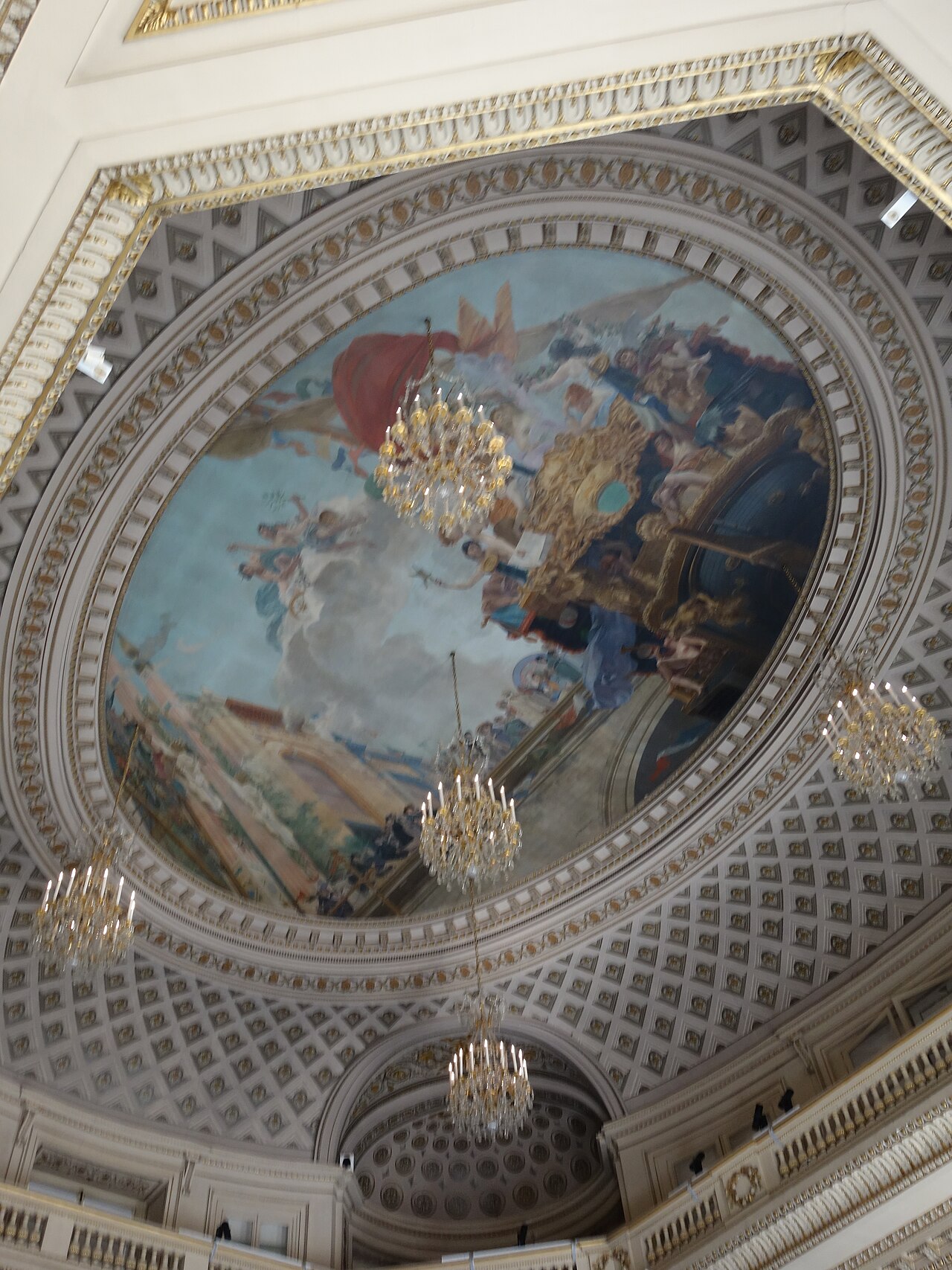 la cupola ovale affrescata di una sala di rappresentanza della monnaie, con una scena allegorica di figure fra le nuvole, la cornice a cassettoni dorati e tre lampadari di cristallo accesi