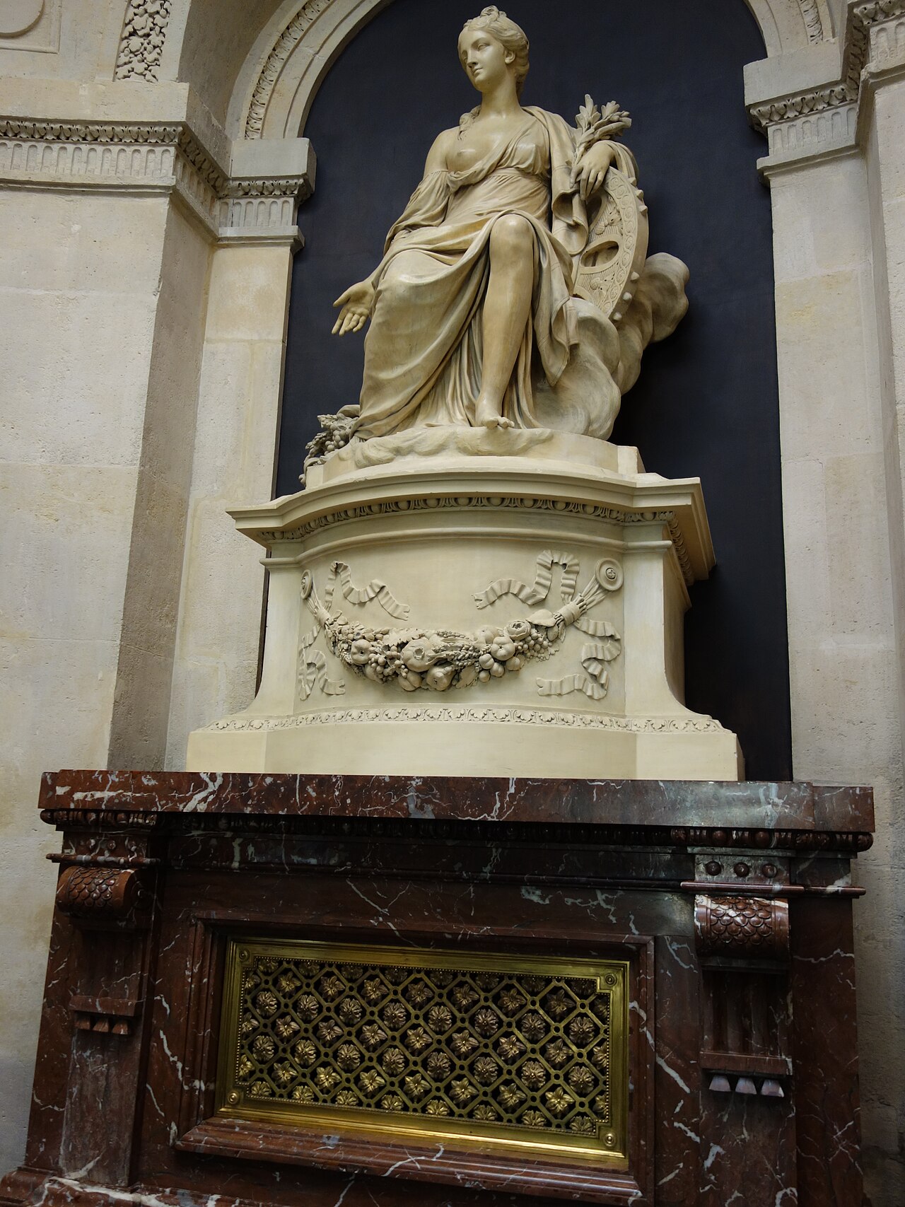 statua allegorica femminile seduta in una nicchia ad arco, con la veste classica, la cornucopia sul braccio sinistro e una grande ruota decorata alle spalle, sopra un camino di marmo rosso venato