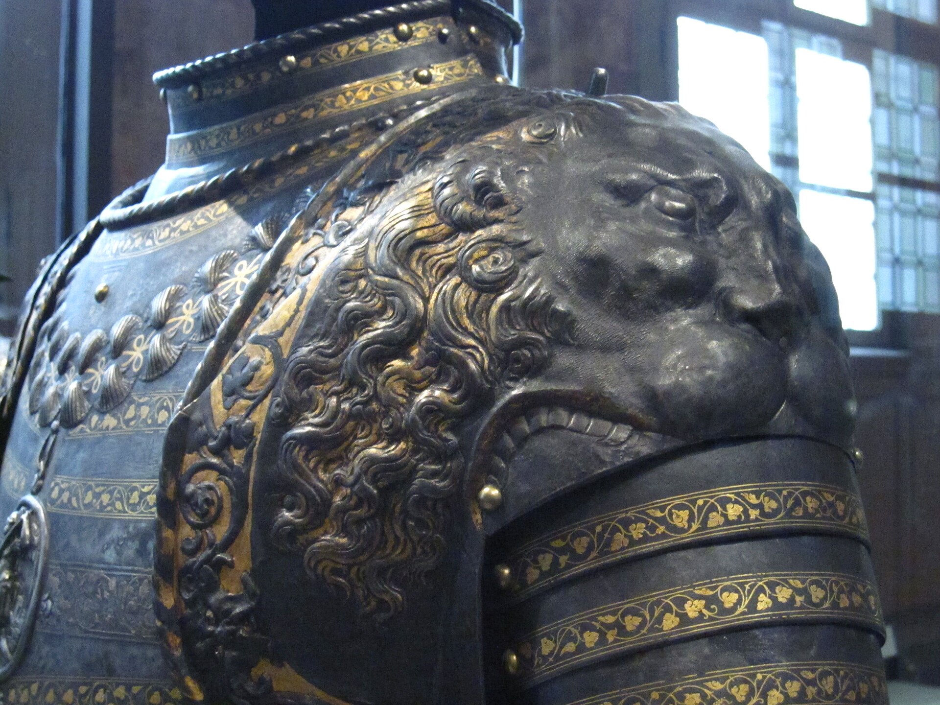 l epaule de l armure aux lions de negroli au musee de l armee, avec une tete de lion repoussee dans le metal sombre et des bandes decorees d or