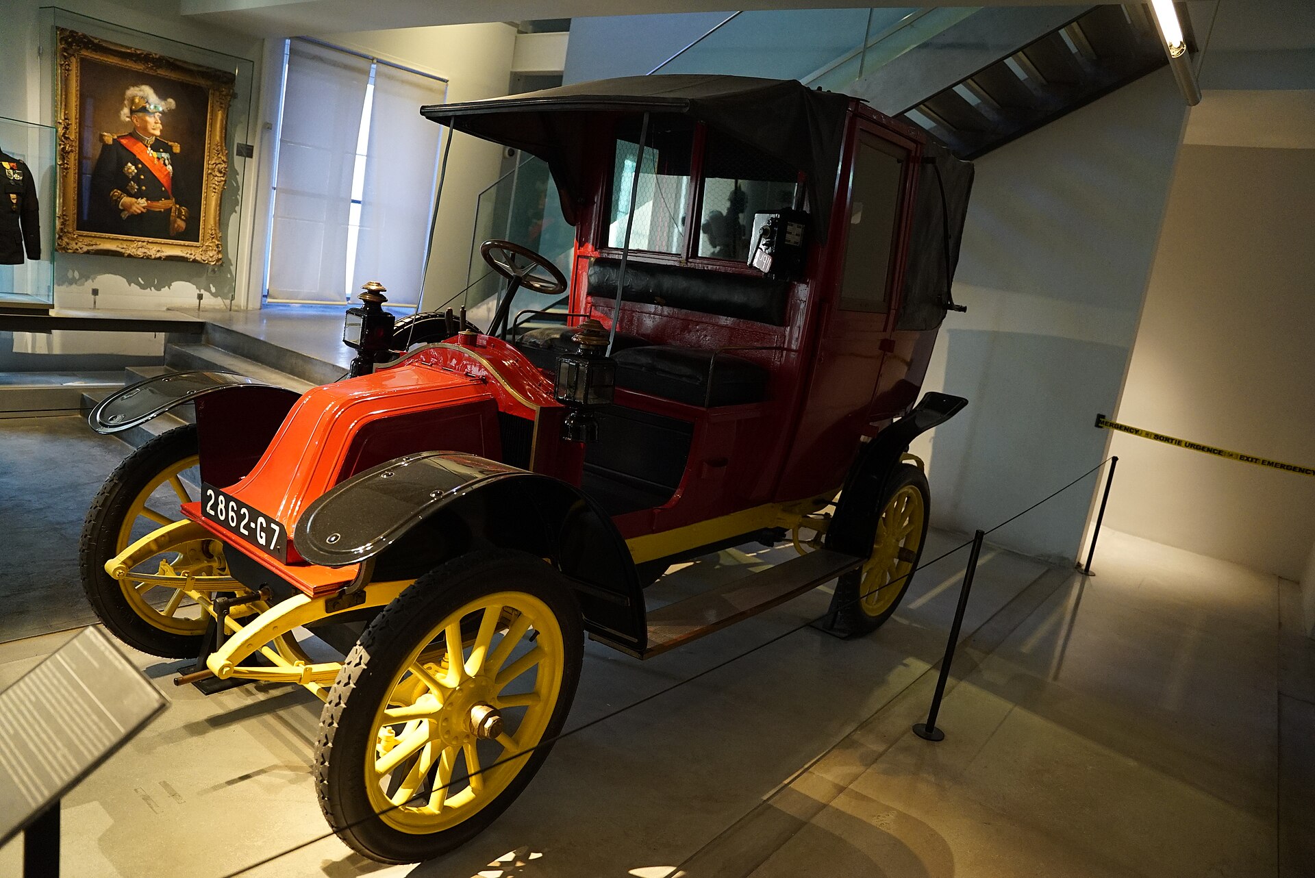 le taxi de la marne au musee de l armee, une petite renault rouge et noire aux roues jaunes, exposee dans une salle avec un portrait au mur