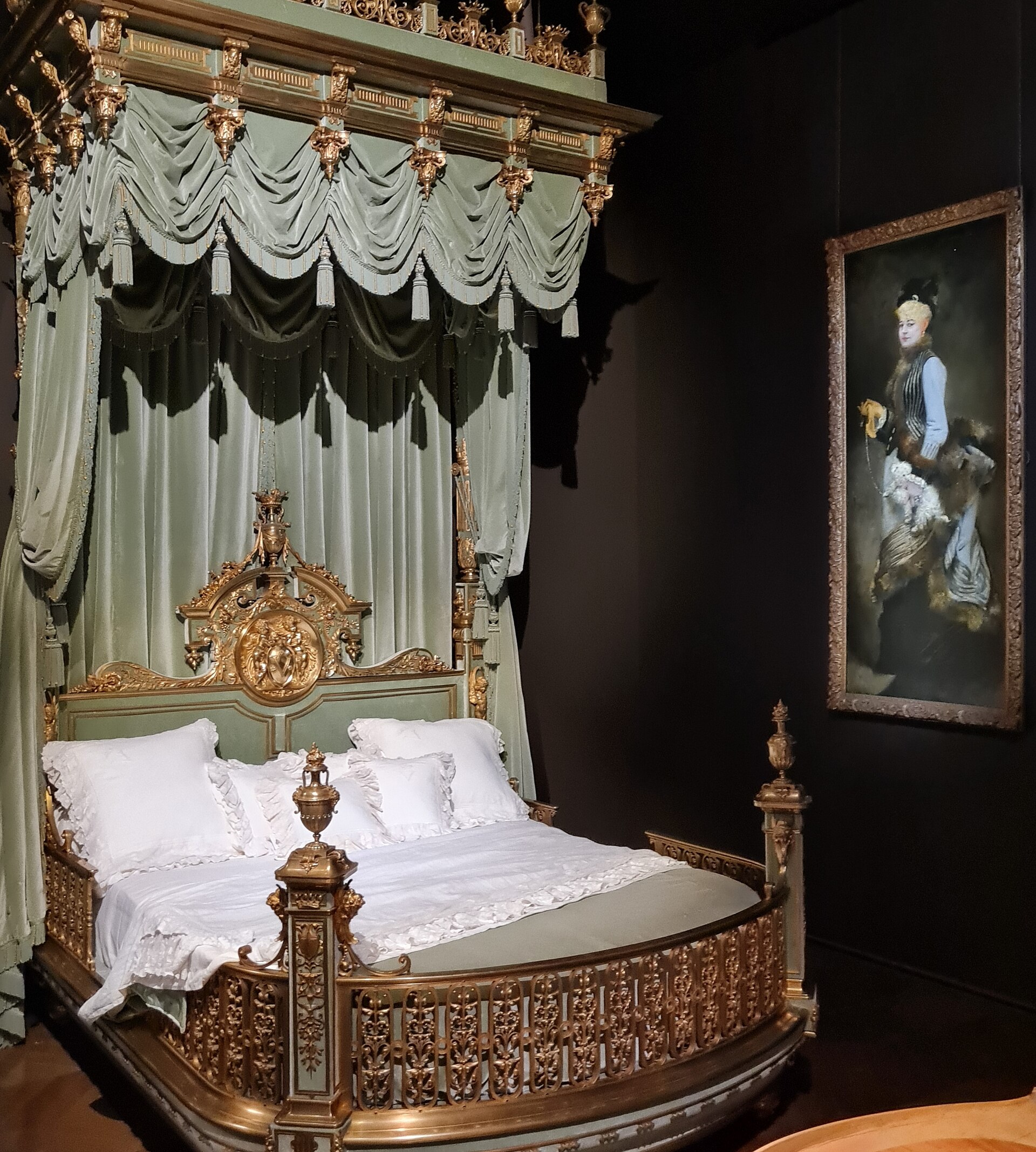 le lit de parade de valtesse de la bigne au musee des arts decoratifs, avec le baldaquin de soie vert pale, la structure de bronze dore et un portrait accroche au mur sombre