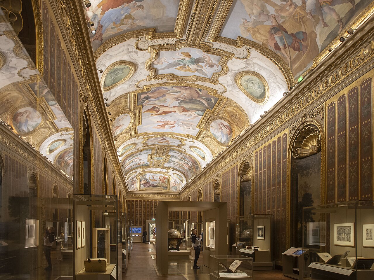 la galerie mazarin in prospettiva, con la volta a botte affrescata entro cornici dorate, le pareti a broccato e le vetrine del museo lungo il corridoio, con un grande globo al centro