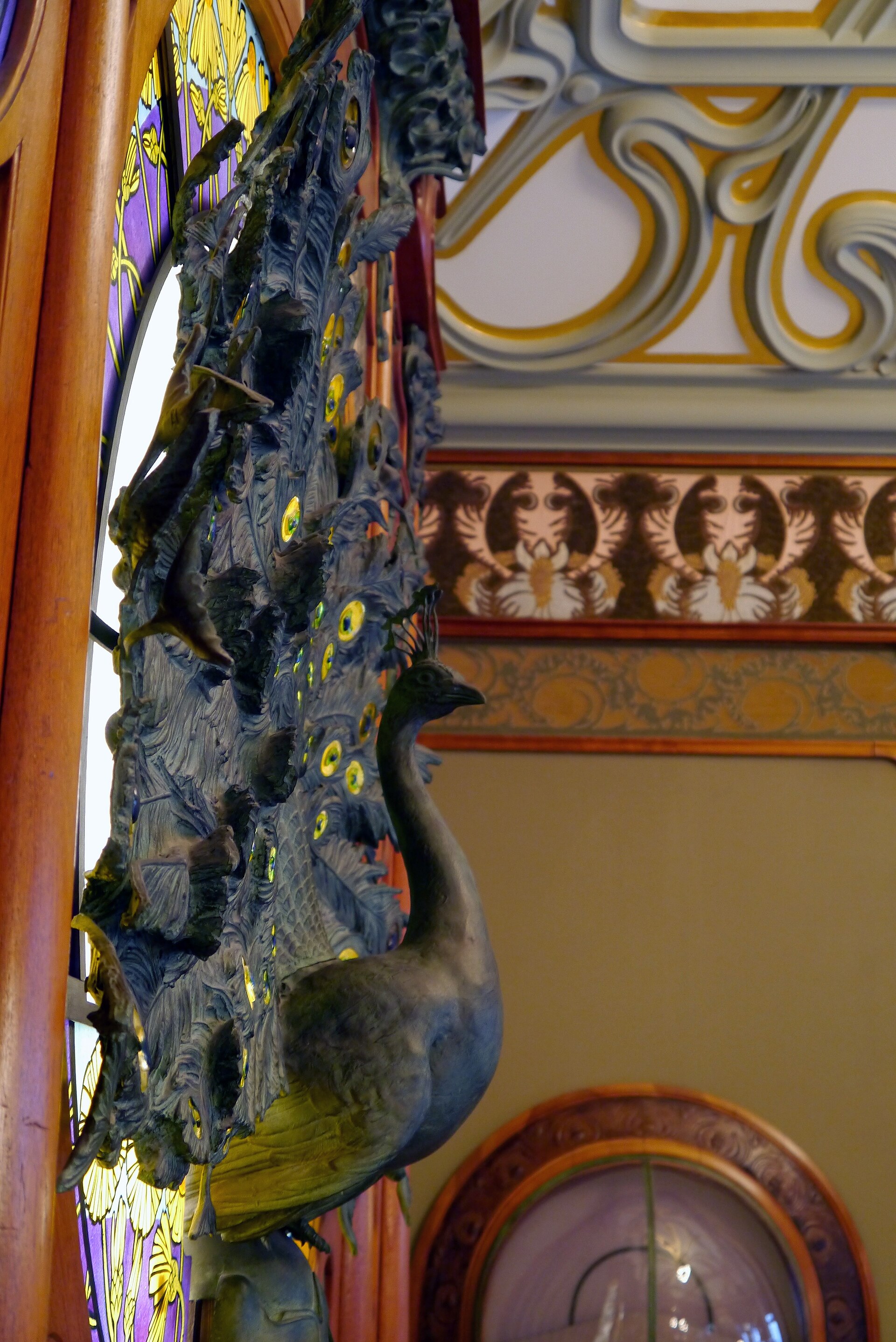 il pavone di bronzo della gioielleria fouquet al musee carnavalet, davanti a una vetrata art nouveau gialla e viola, con il soffitto a stucchi bianchi e dorati