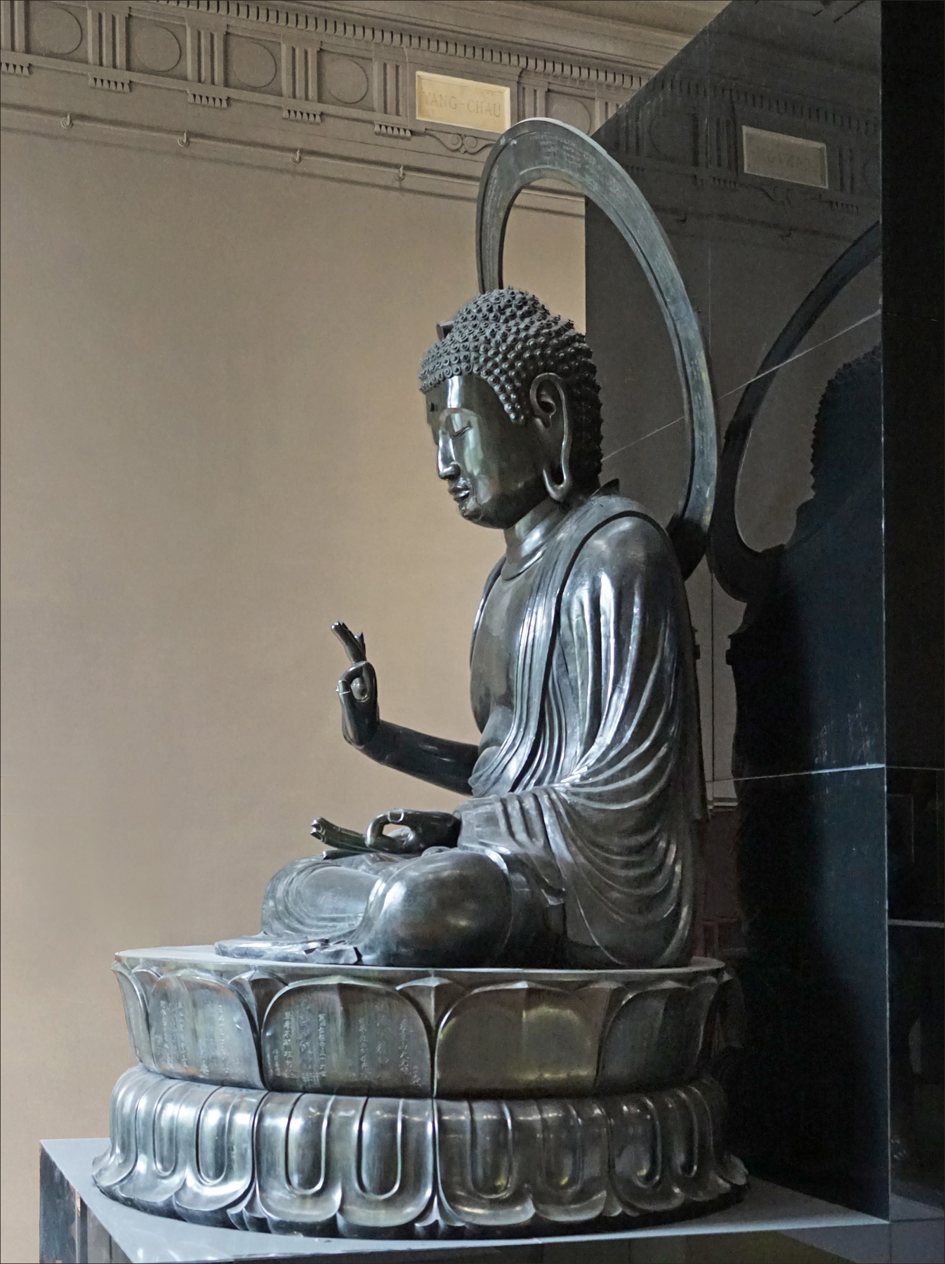 il grande buddha amida in bronzo del musee cernuschi visto di profilo, seduto a gambe incrociate su un doppio loto con la mano destra alzata