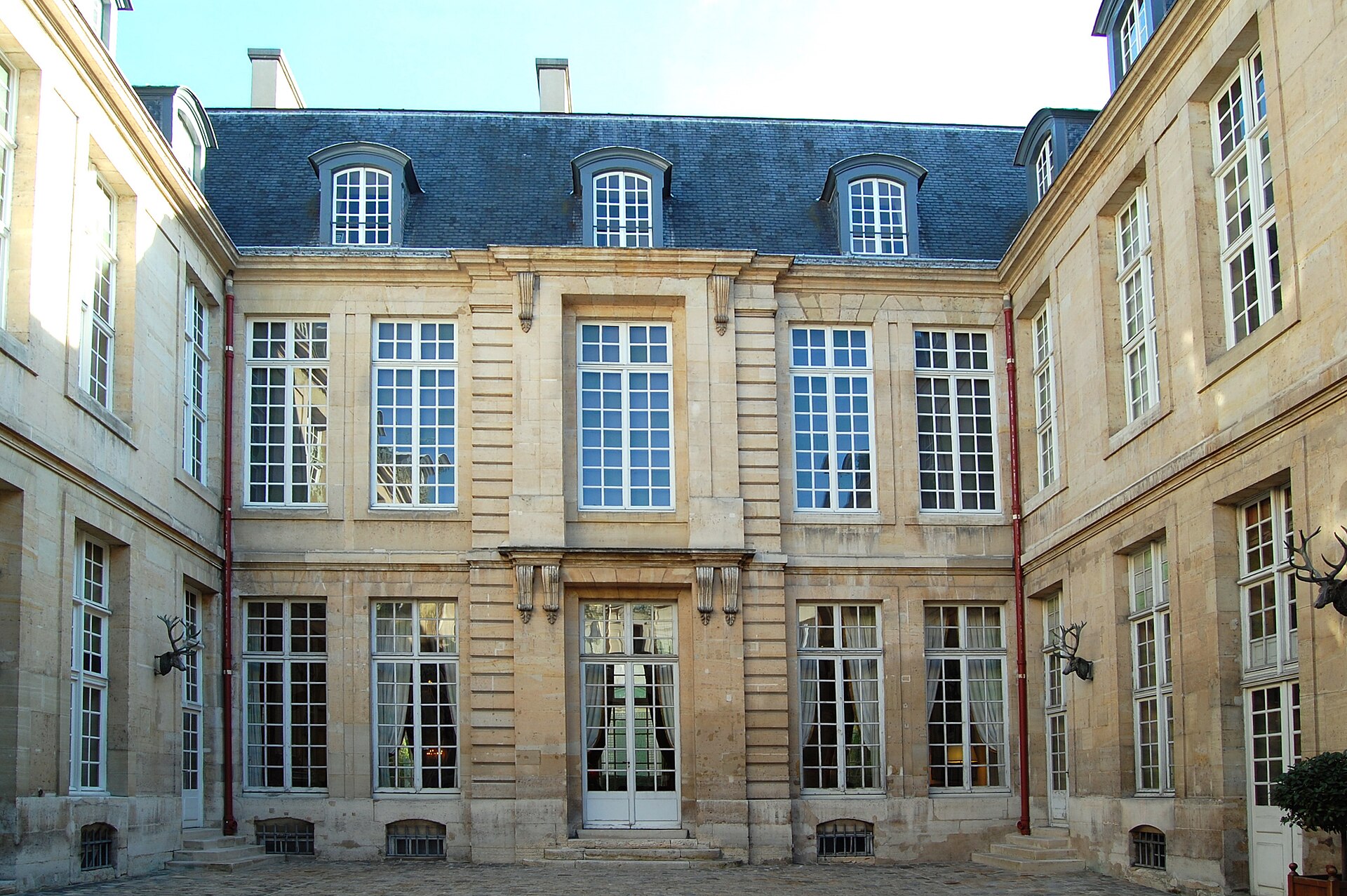 il cortile dell hotel de guenegaud a parigi, con la facciata di pietra chiara a bugnato, le finestre alte e due teste di cervo di bronzo appese ai muri laterali
