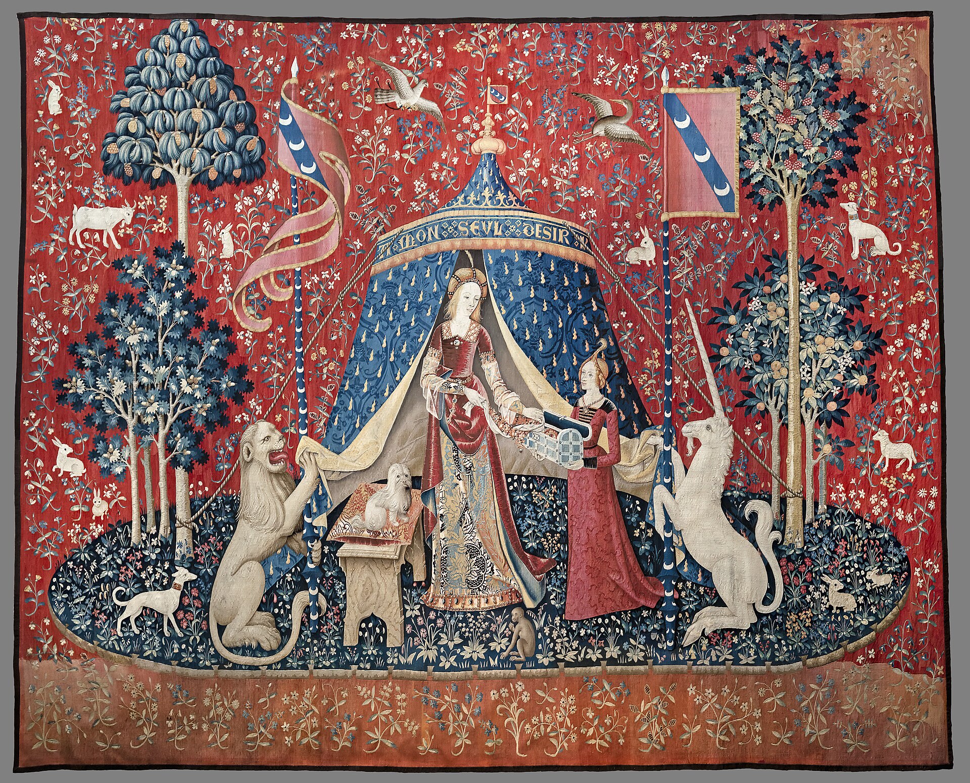 the mon seul desir tapestry of the lady and the unicorn, on a red millefleurs ground, with the lady under a blue tent between a lion and a unicorn holding two banners