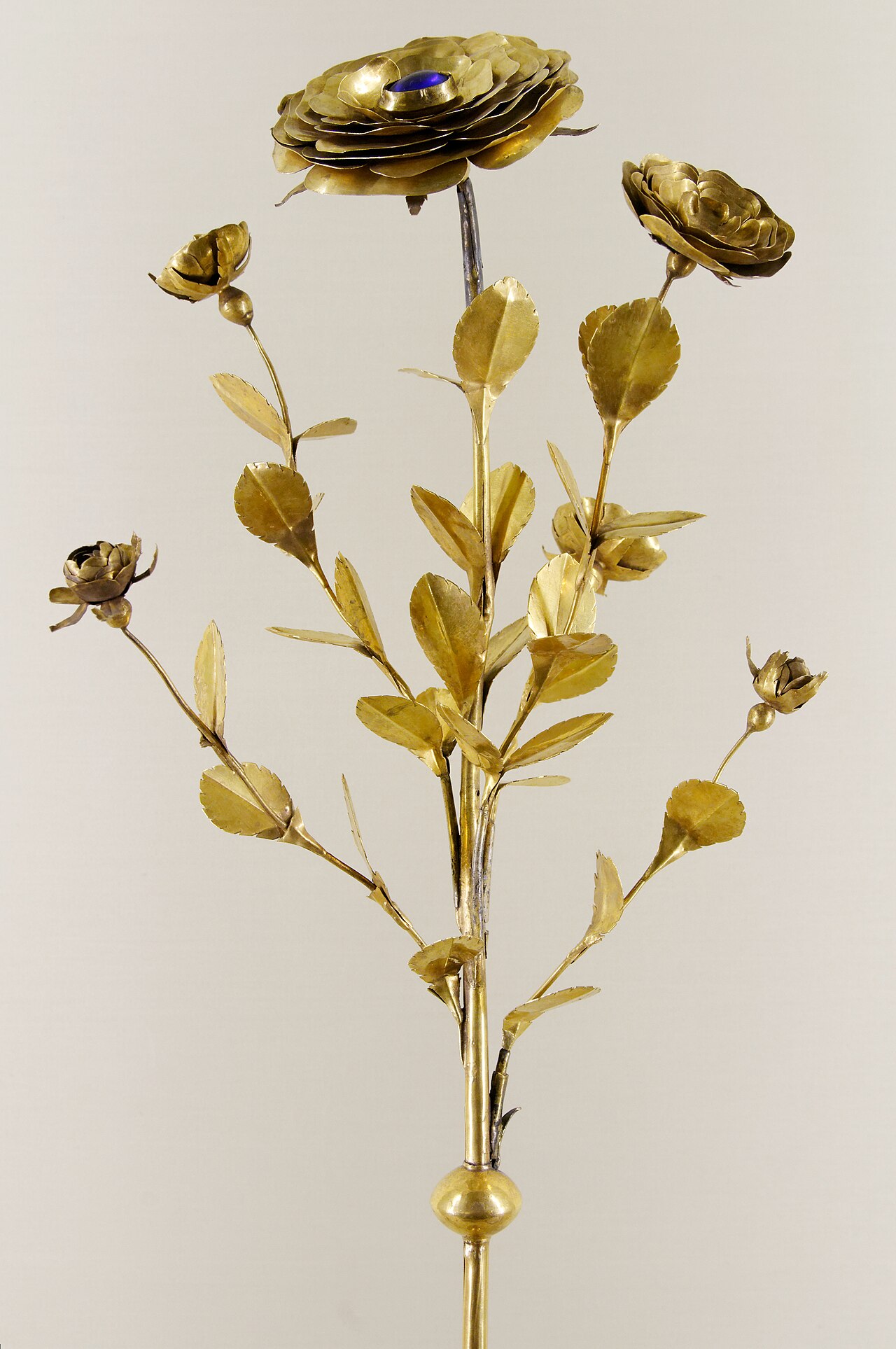 the golden rose of basel at the musee de cluny, a golden rose bush with a large rose at the top set with a blue stone, buds and serrated leaves