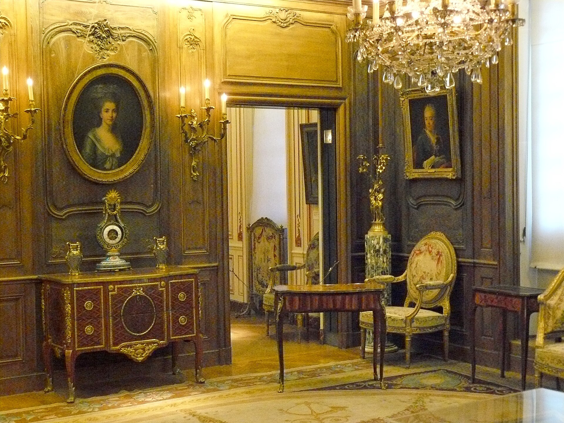 una sala del musee cognacq jay con le boiserie chiare, un ritratto ovale femminile, una consolle intarsiata e un lampadario di cristallo