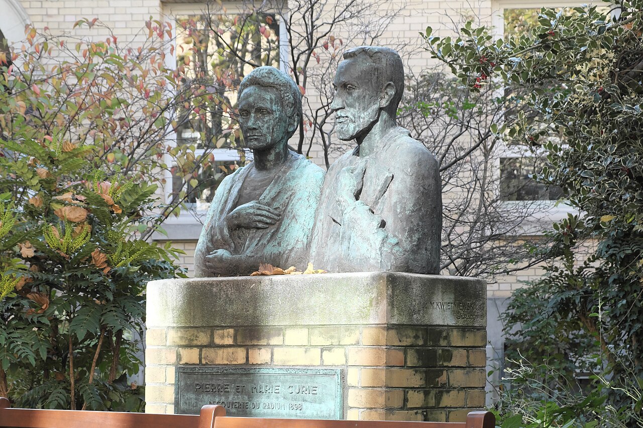 il monumento in bronzo a doppio busto di pierre e marie curie nel giardino, su un basamento di mattoni con la targa pierre et marie curie decouverte du radium 1898, fra arbusti autunnali