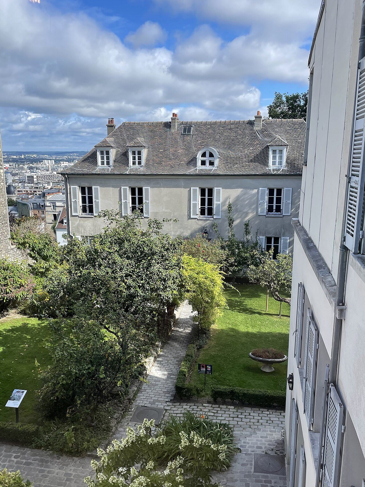 la maison du bel air vista dall alto, con il tetto di tegole e gli abbaini, le persiane grigio azzurro, i jardins renoir davanti e la distesa dei tetti di parigi fino all orizzonte sulla sinistra