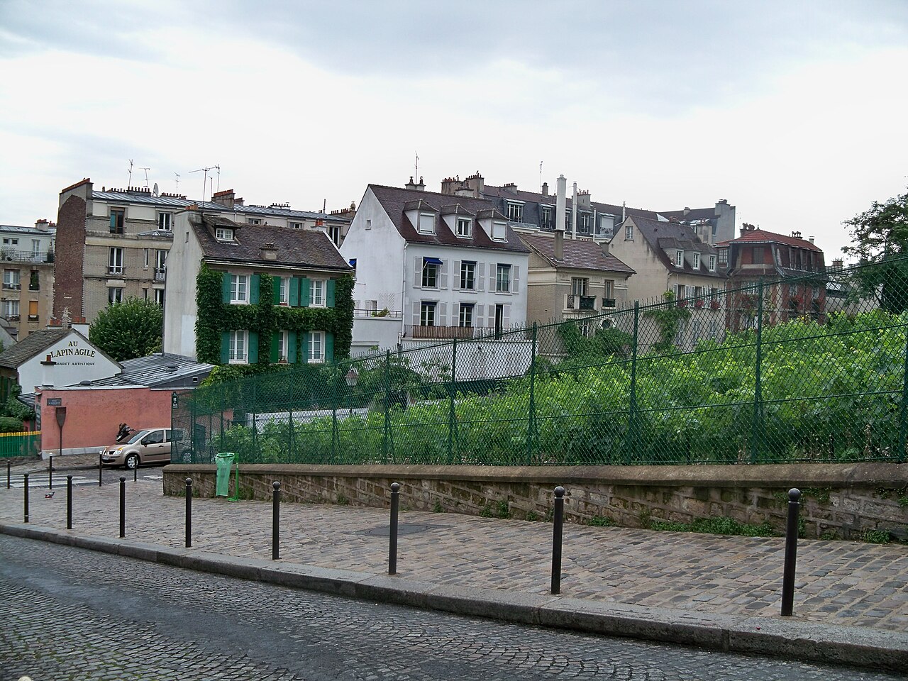 la vigna di montmartre vista dalla strada, con i filari in pendenza dietro la recinzione e la casetta del cabaret lapin agile sull angolo, in basso