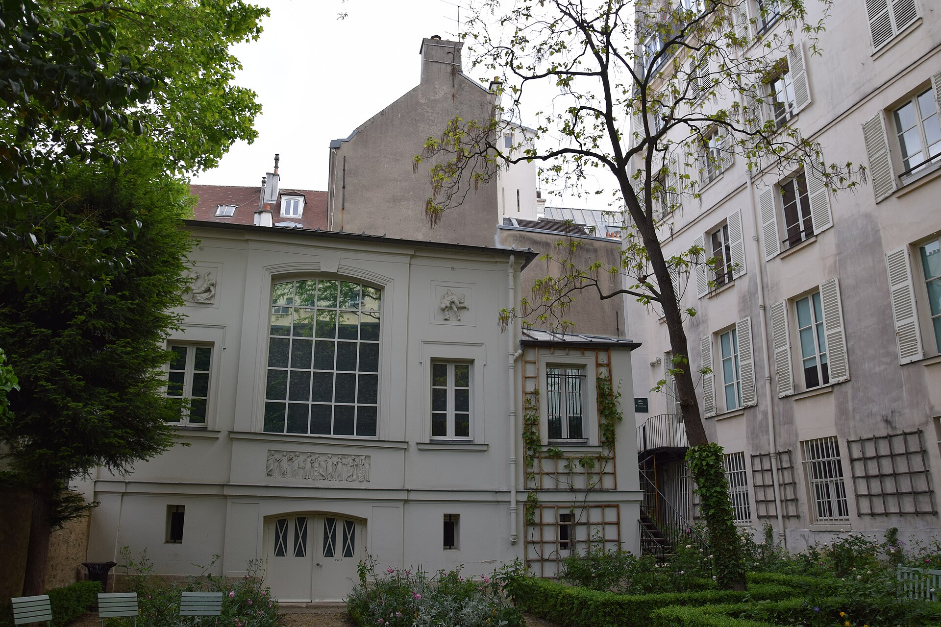 delacroix studio seen from the garden, a low grey green building with a large gridded window, reliefs set into the wall and box hedges in front