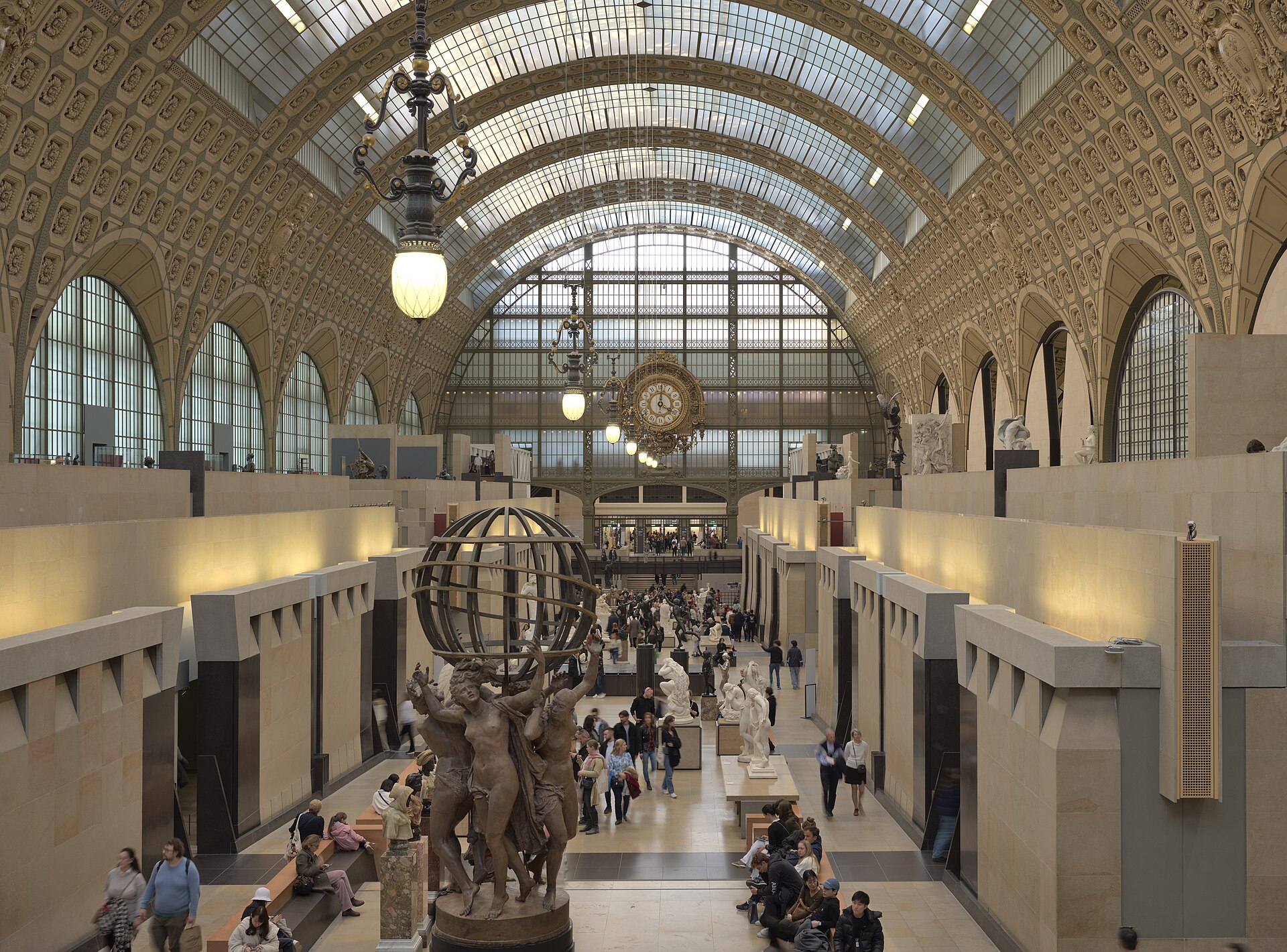 la nef du musee d orsay vue d en haut, avec la verriere de fer et de verre de l ancienne gare, les sculptures le long de l allee centrale et la grande horloge doree au fond