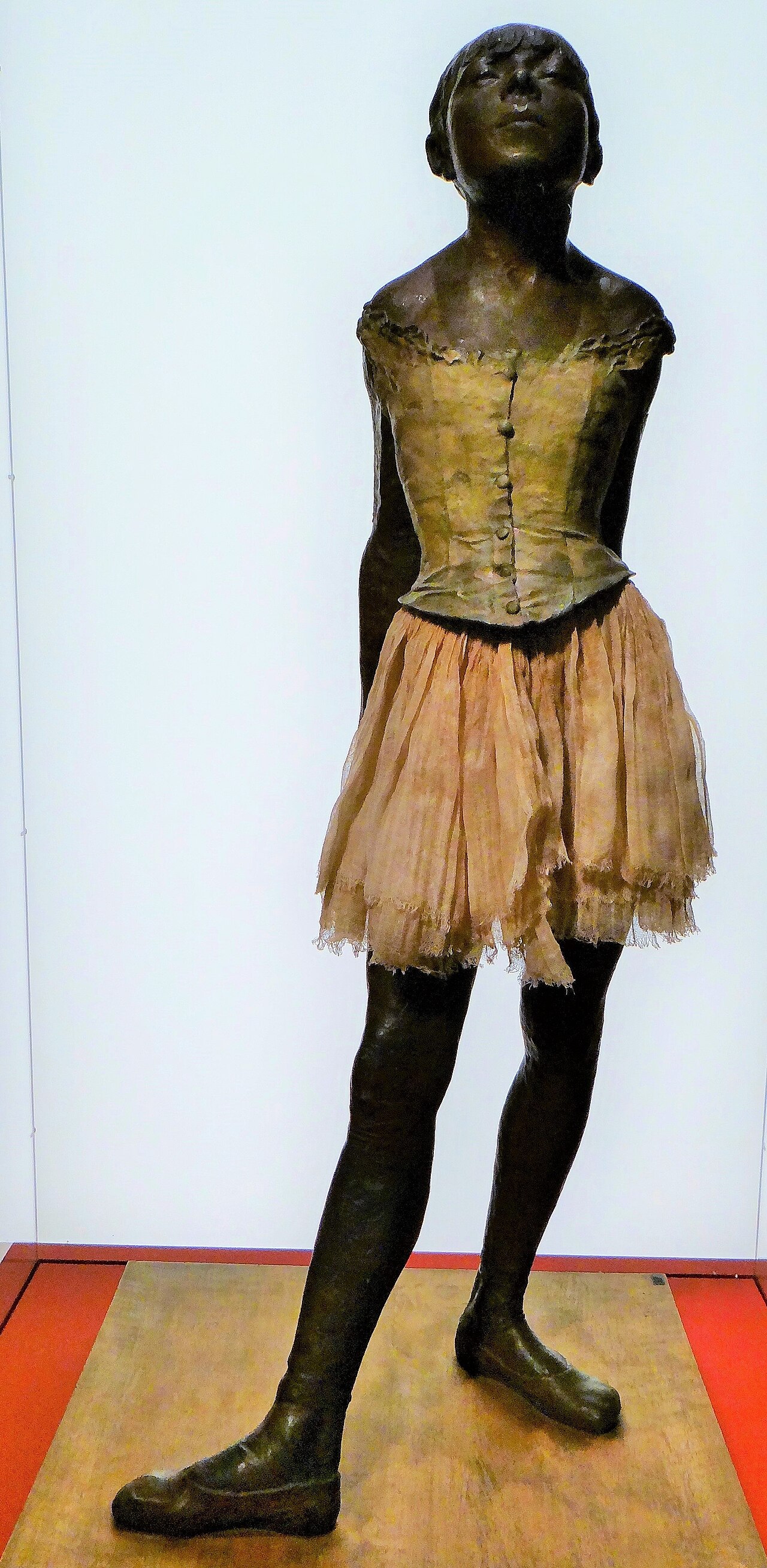 la petite danseuse de quatorze ans de degas, une statue de bronze sombre d une jeune fille debout les mains derriere le dos, le menton leve et un vrai tutu de tulle a la taille