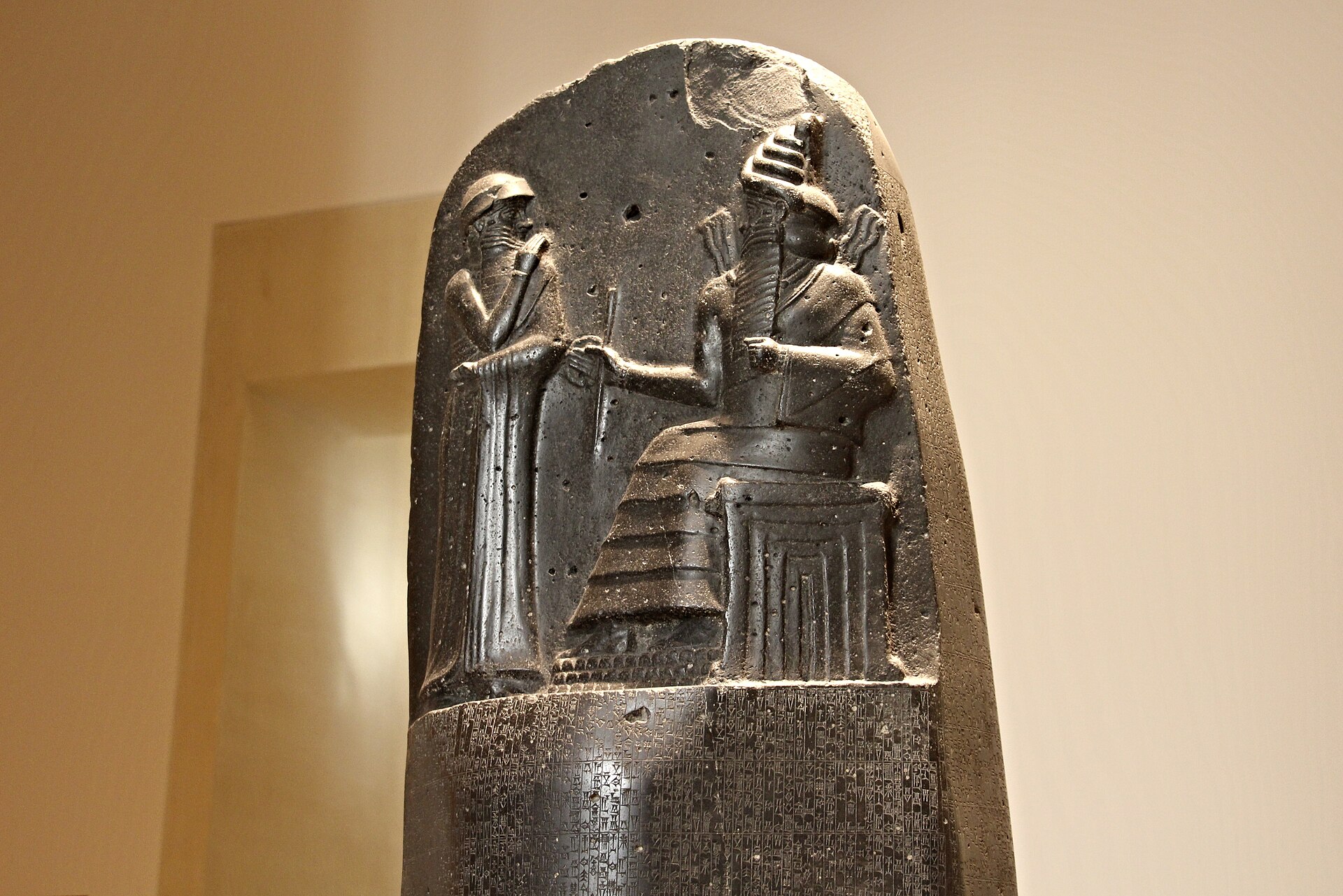 le haut de la stele du code de hammurabi au louvre, avec le relief du roi debout devant le dieu shamash assis sur son trone et les premieres lignes d ecriture cuneiforme
