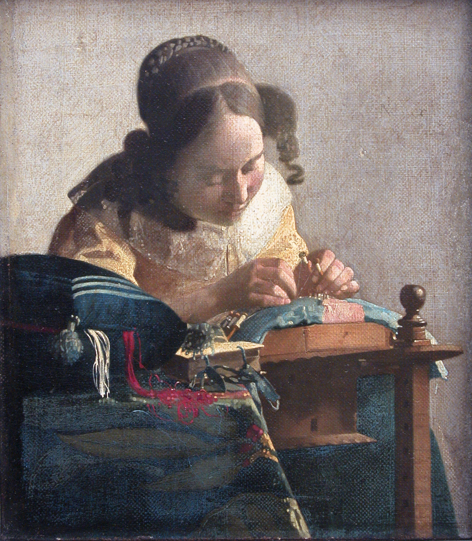 la dentelliere de vermeer, une jeune femme penchee sur son ouvrage avec les fuseaux entre les doigts, un coussin de couture au premier plan d ou sortent des fils rouges et blancs