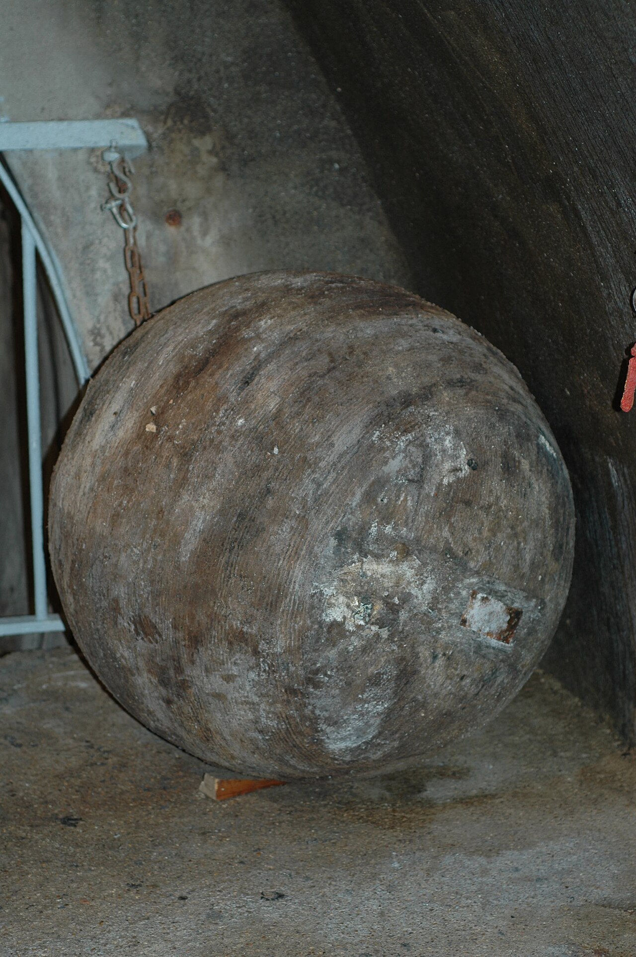 primo piano della boule de curage, la grossa sfera scura usata per pulire le condotte per abrasione, appesa alla sua catena davanti alla parete della galleria