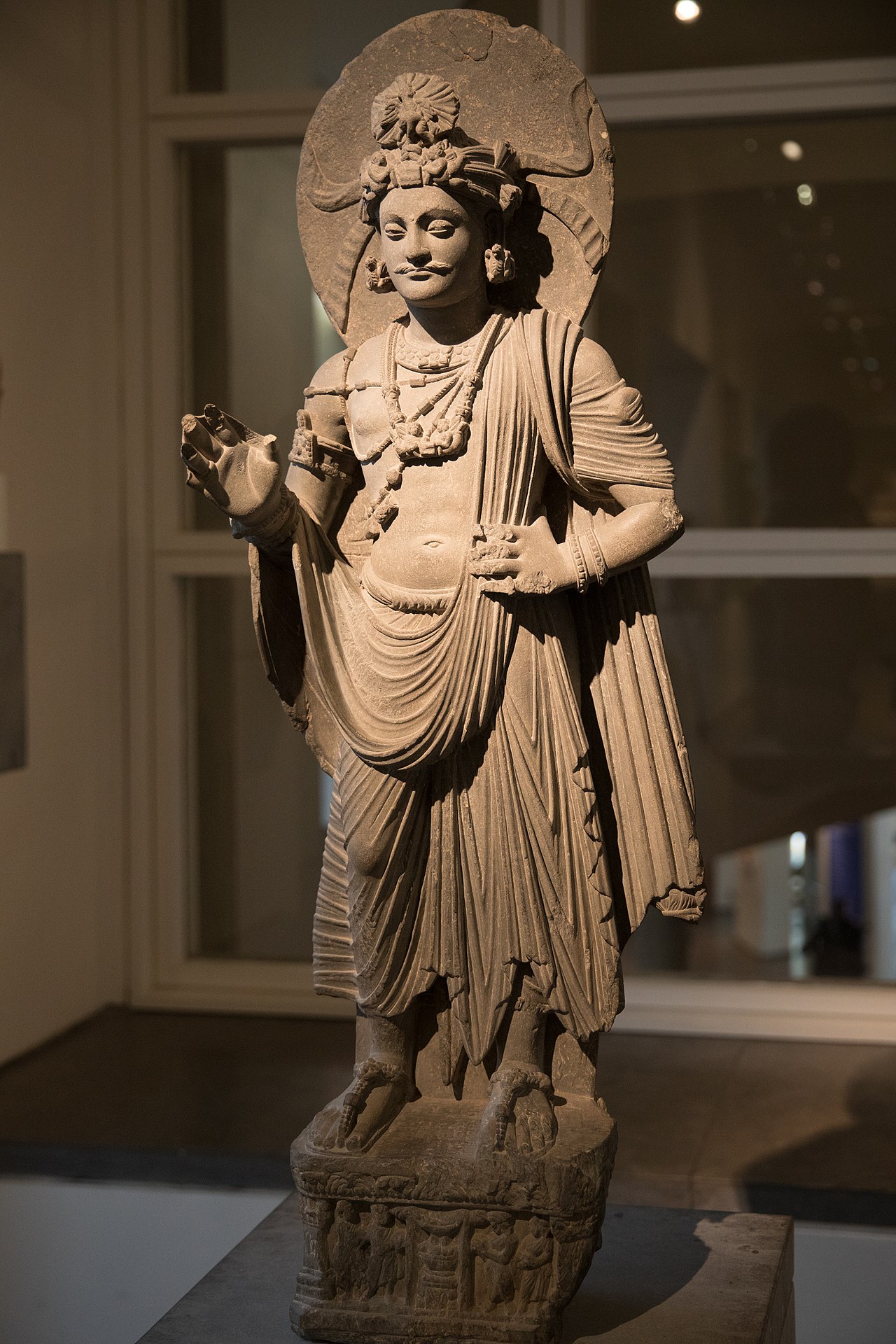 la statua in arenaria di un bodhisattva del gandhara al musee guimet, in piedi con l aureola dietro la testa, i baffi, le collane e il panneggio a pieghe profonde