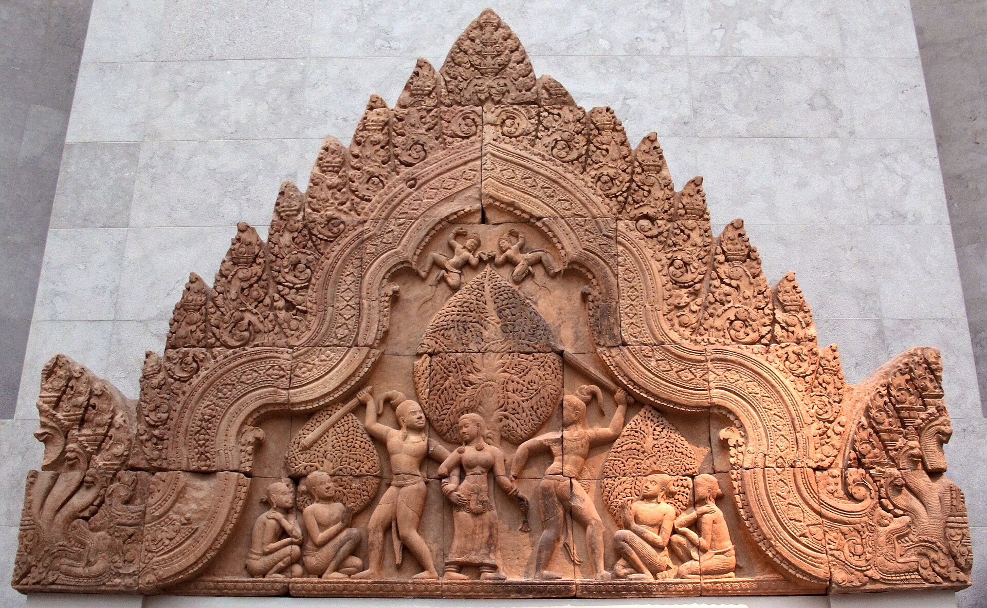 il frontone in arenaria rosa di banteay srei al musee guimet, un arco a fiamme con due uomini che alzano la clava ai lati di una donna in piedi e figure sedute in basso