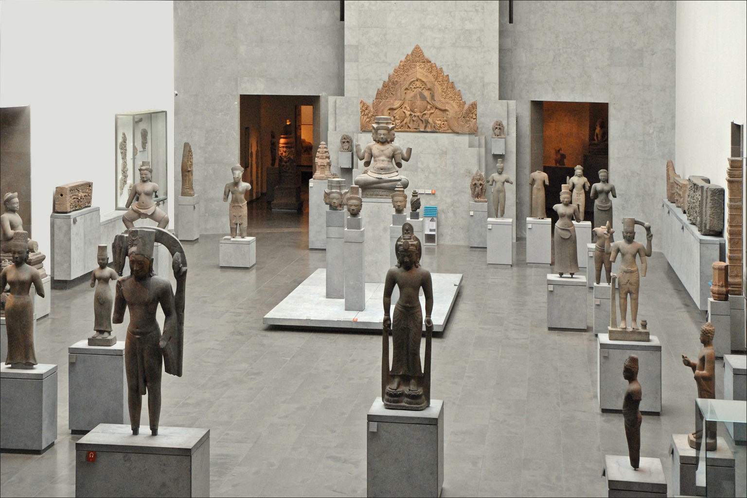 la galleria khmer del musee guimet, decine di sculture in arenaria su zoccoli bianchi in una sala grigia, con un frontone scolpito montato sulla parete in fondo
