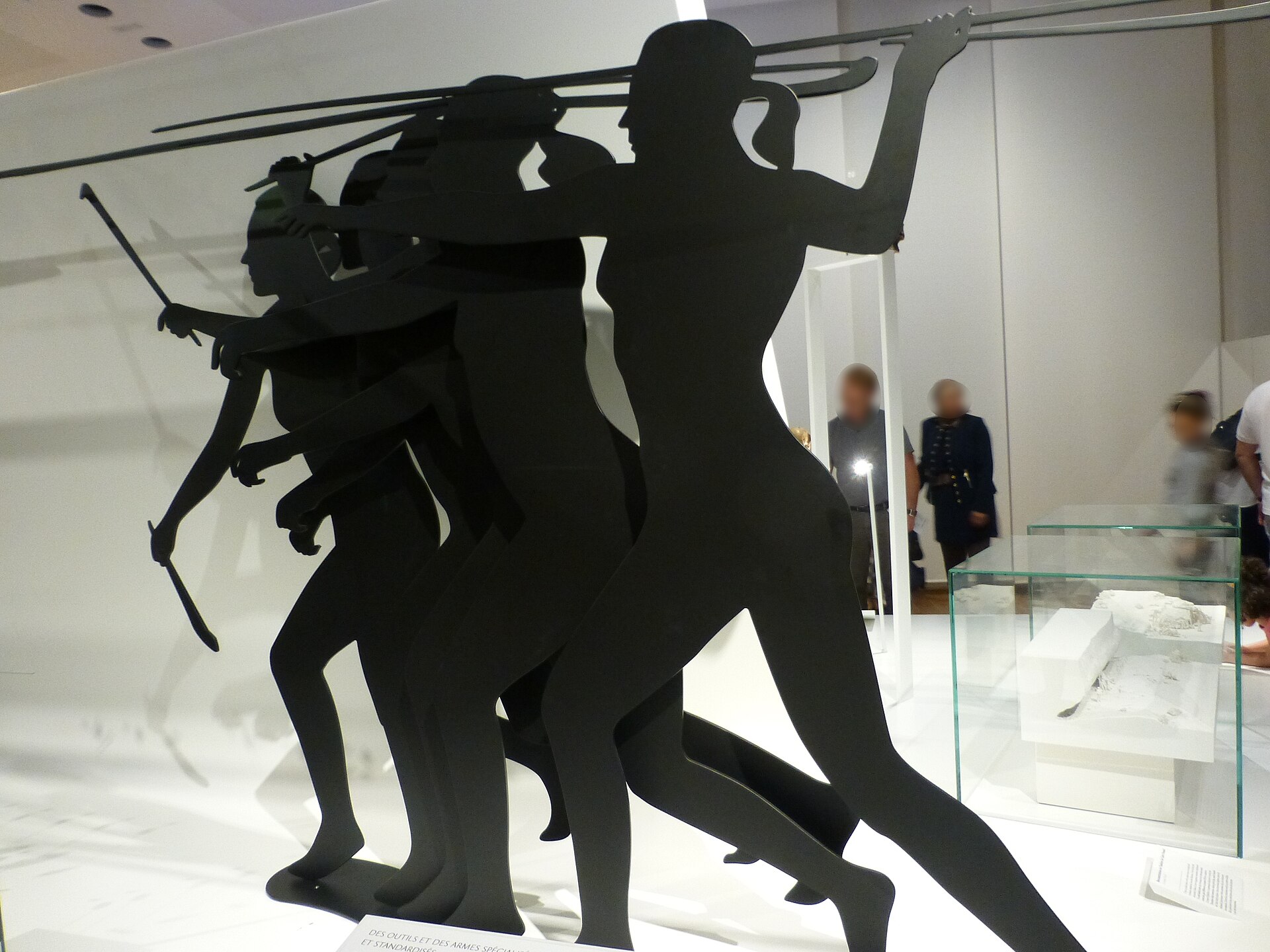 le sagome nere a grandezza naturale di tre cacciatori preistorici che lanciano zagaglie con il propulsore, in una sala bianca del musee de l homme
