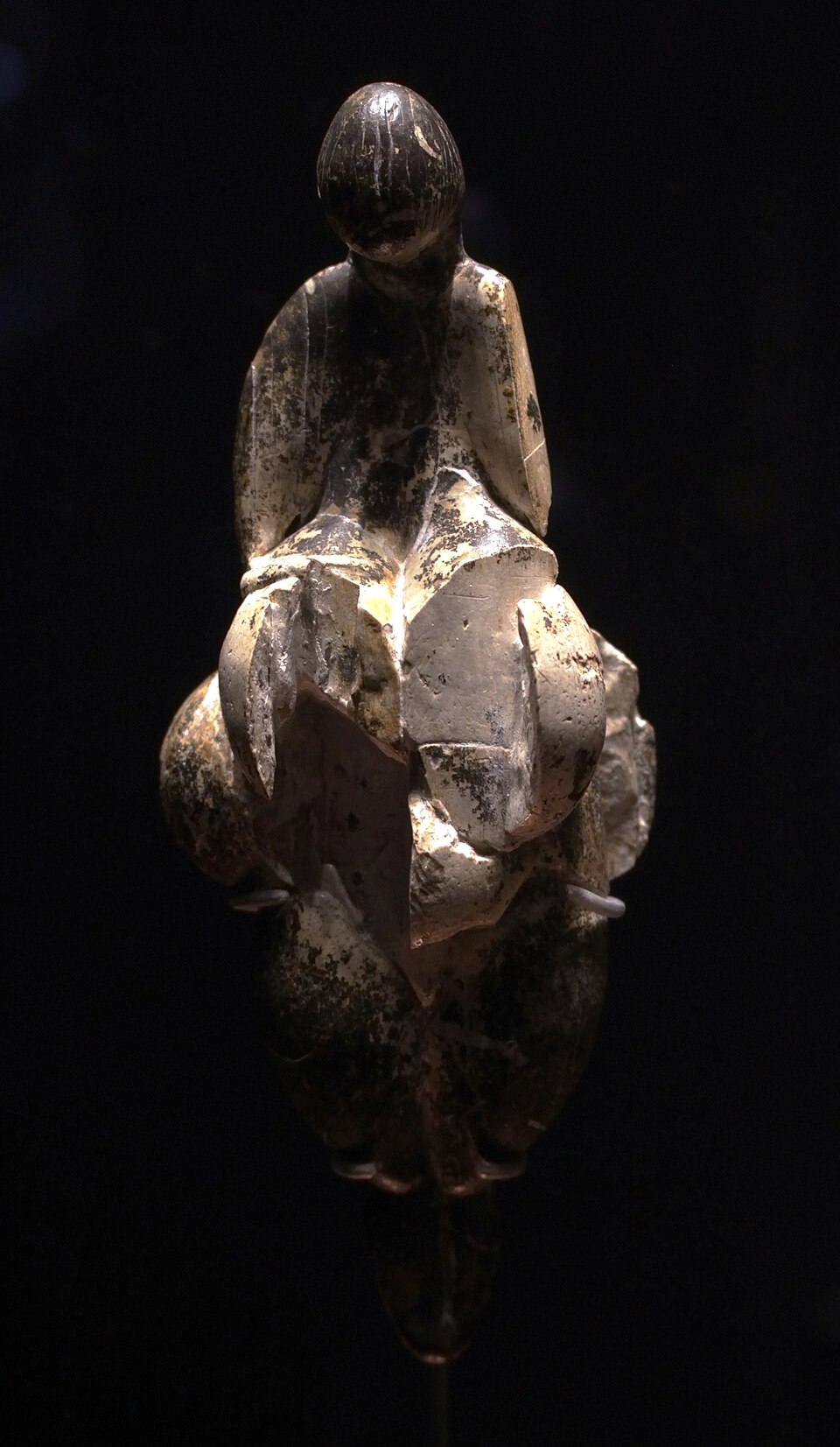 la venere di lespugue al musee de l homme, la statuetta in avorio di mammut con la testa piccola e liscia e il corpo a losanga, illuminata su fondo nero