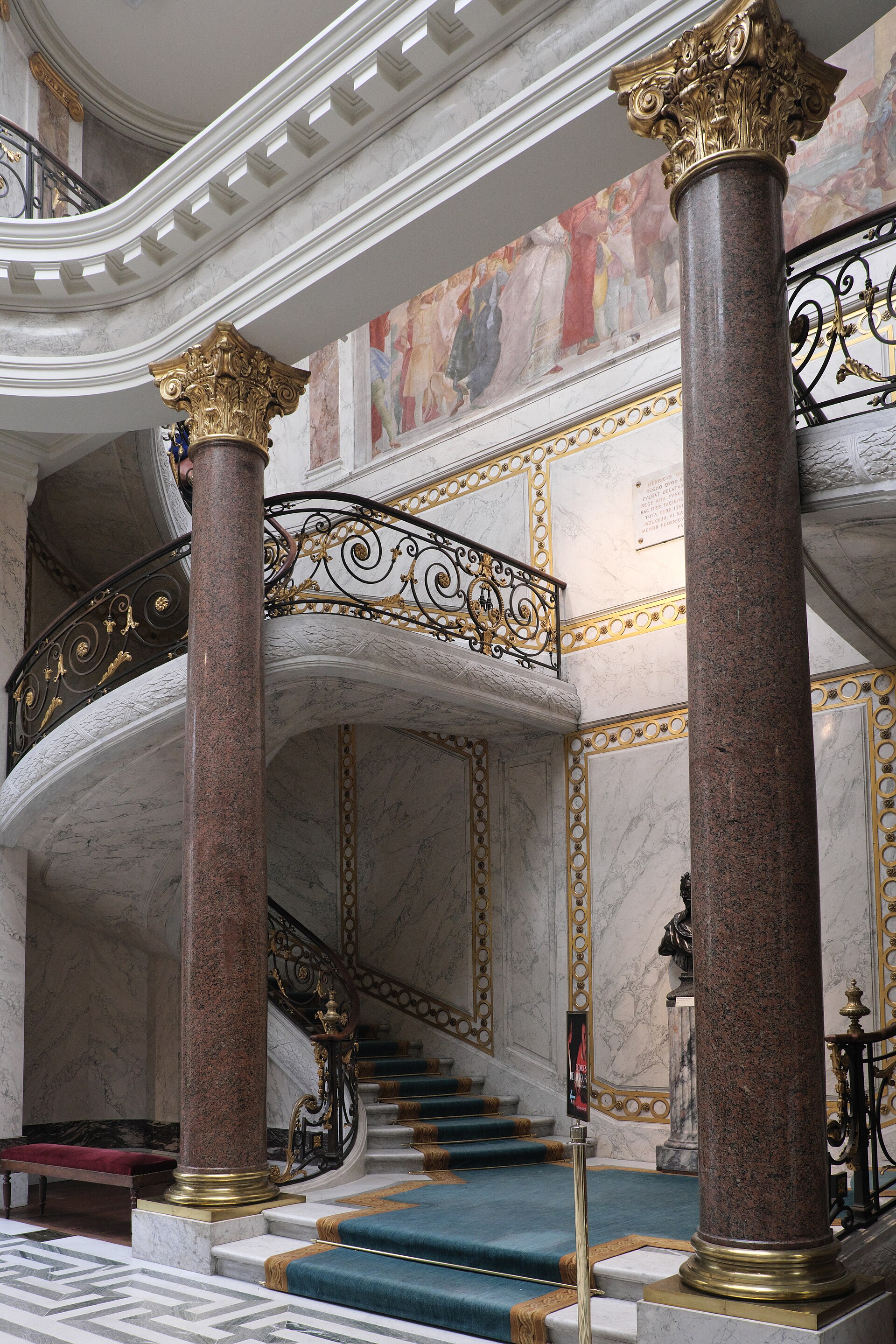 lo scalone monumentale del musee jacquemart andre fra due colonne di granito rosso, con la balaustra nera e oro e l affresco di tiepolo sulla parete