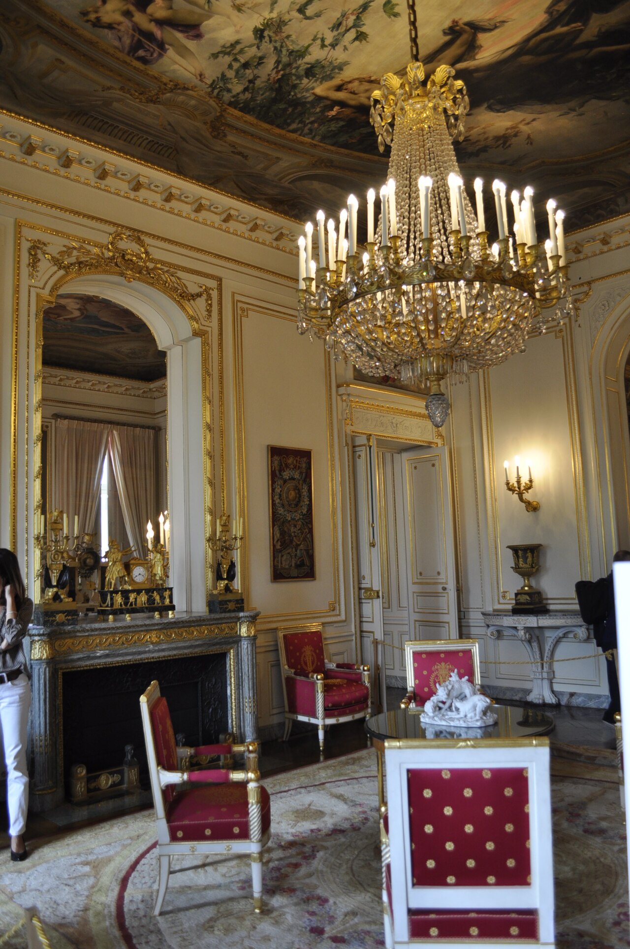 il salone dell aurora con il soffitto interamente dipinto, un grande lampadario di cristallo a decine di candele, lo specchio dorato sopra il camino di marmo grigio con l orologio e i candelabri dorati, e le sedie impero rosse e bianche