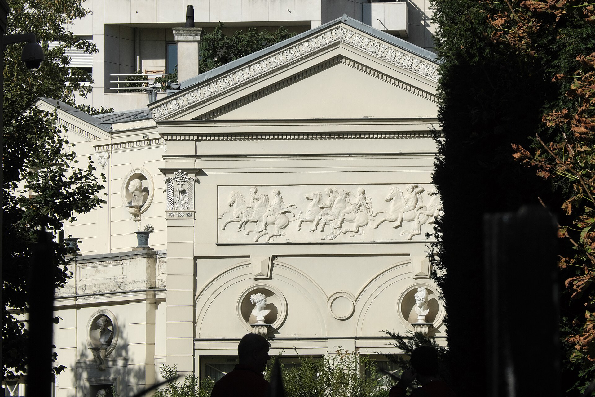 la facciata del musee marmottan monet sul lato del giardino, in pietra chiara con festoni scolpiti, il tetto di ardesia con gli abbaini e lo stendardo verde del museo davanti alla siepe