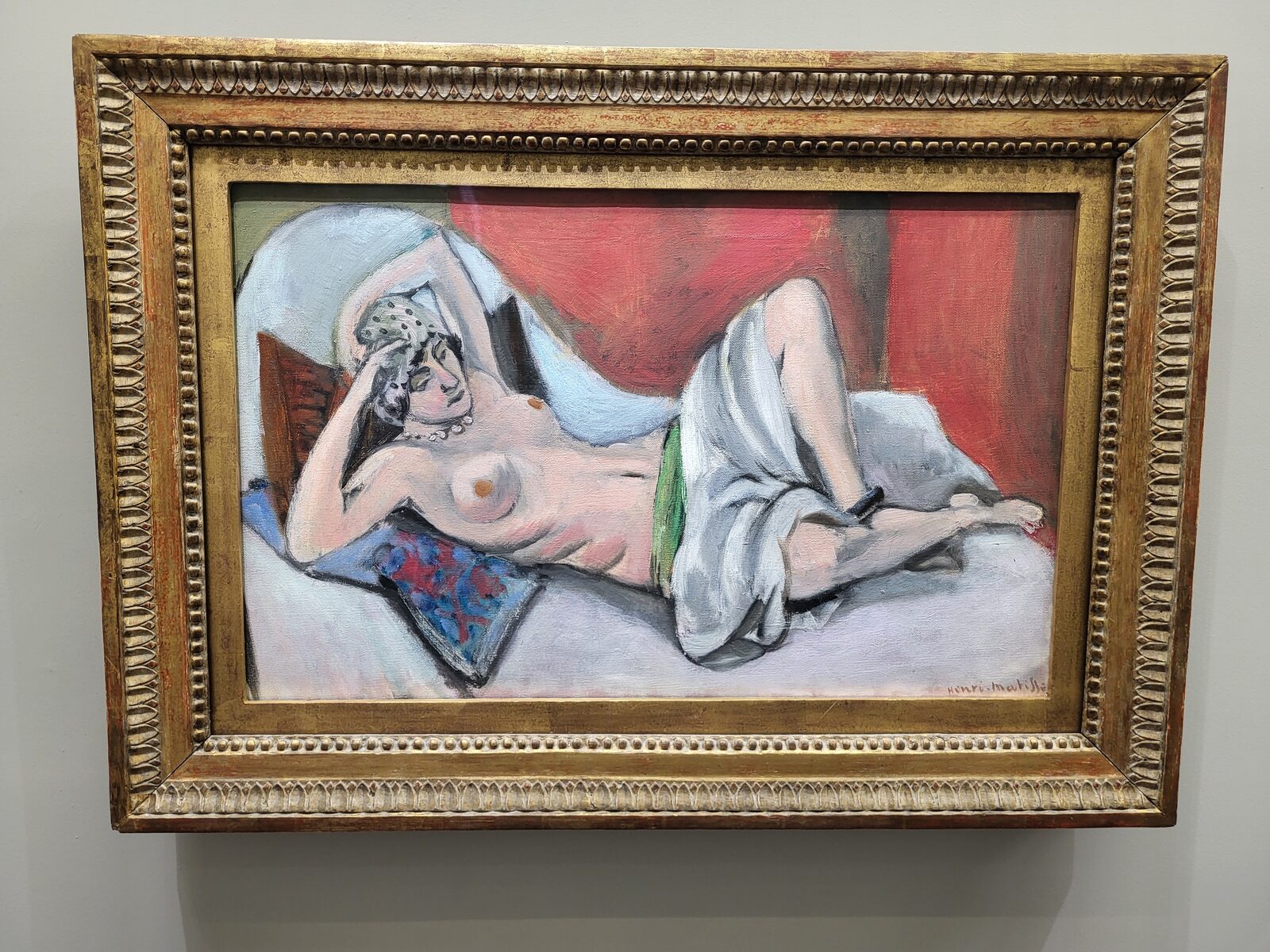 un’odalisca sdraiata di Matisse su fondo rosso, con il panneggio bianco e il cuscino a fiori blu